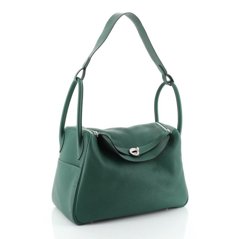 This Hermes Lindy Handbag Clemence 30, crafted in Malachite green Clemence leather, features dual-rolled handles, two sides slip pockets, a connecting long strap and palladium hardware. Its turn-lock and top-zipper closure open to a Malachite green
