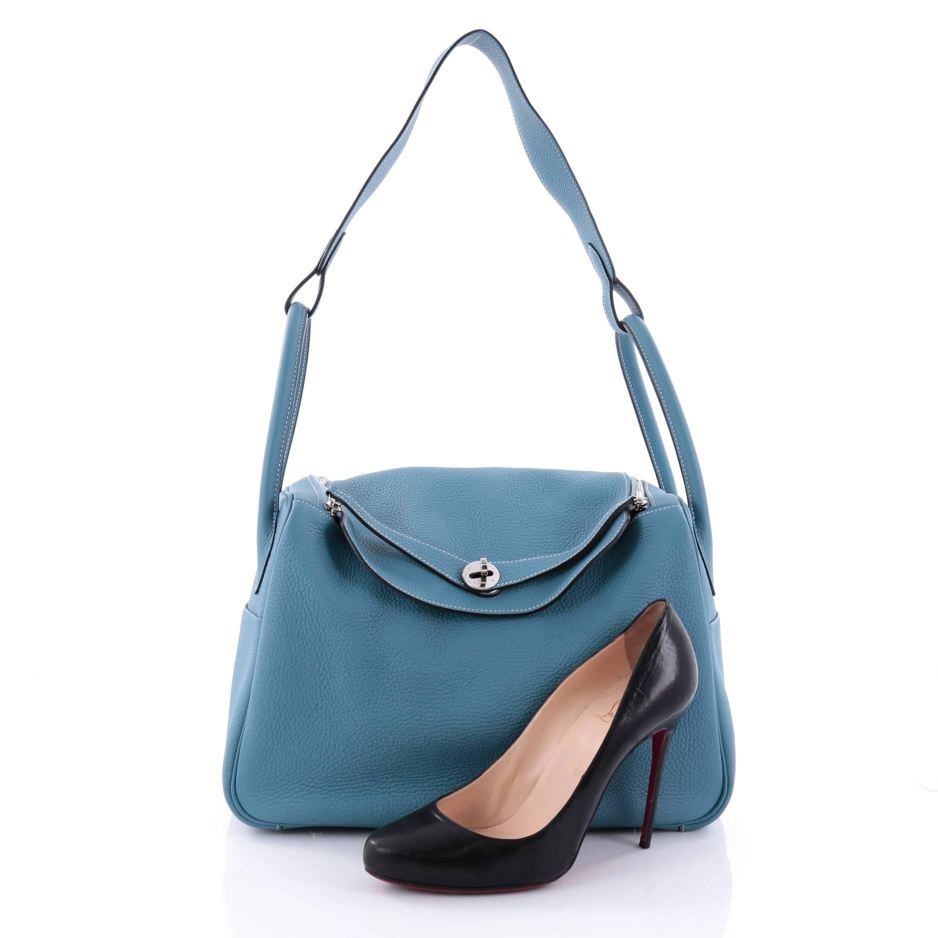 This authentic Hermes Lindy Handbag Clemence 34 is a hard-to-find bag made for Hermes lovers. Crafted from blue jean clemence leather, this chic shoulder bag features dual-rolled handles with a connecting long strap, two side slip pockets,