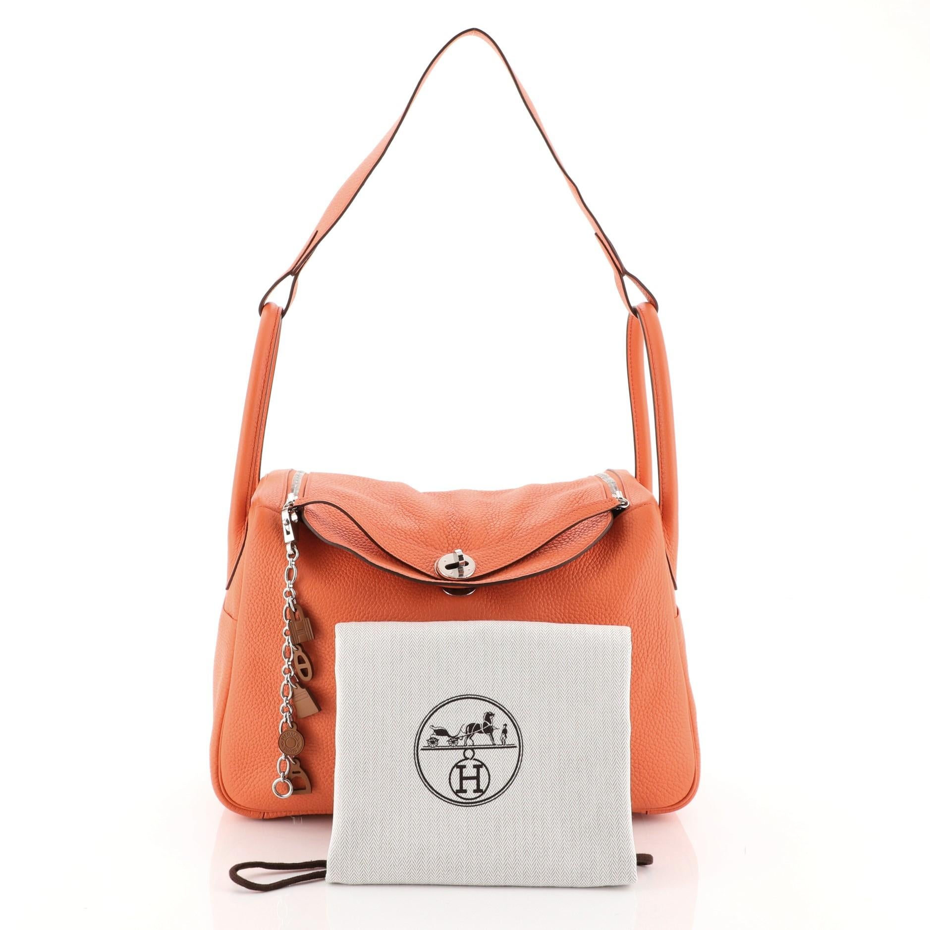 This Hermes Lindy Handbag Clemence 34, crafted from Orange Poppy orange Clemence leather, features dual rolled handles with a connecting long strap, two side slip pockets, protective base studs, and palladium hardware. Its double zip closure opens