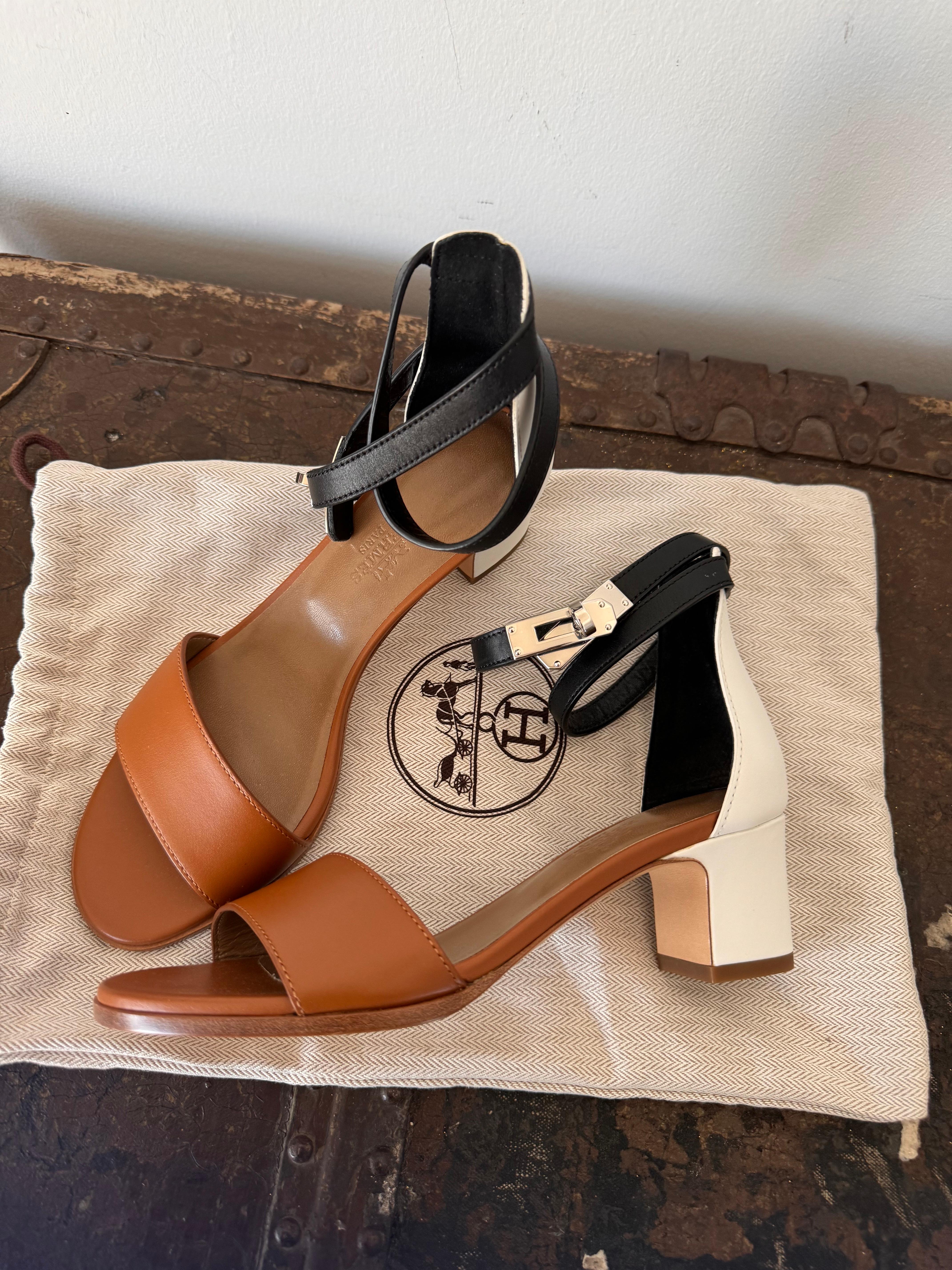 Elevate your footwear collection with the Hermes Mahege Sandal in a striking brown and white color palette, accentuated by a sophisticated black ankle strap and iconic Kelly lock detail. This exquisite sandal, boasting a size 35, is not just a shoe
