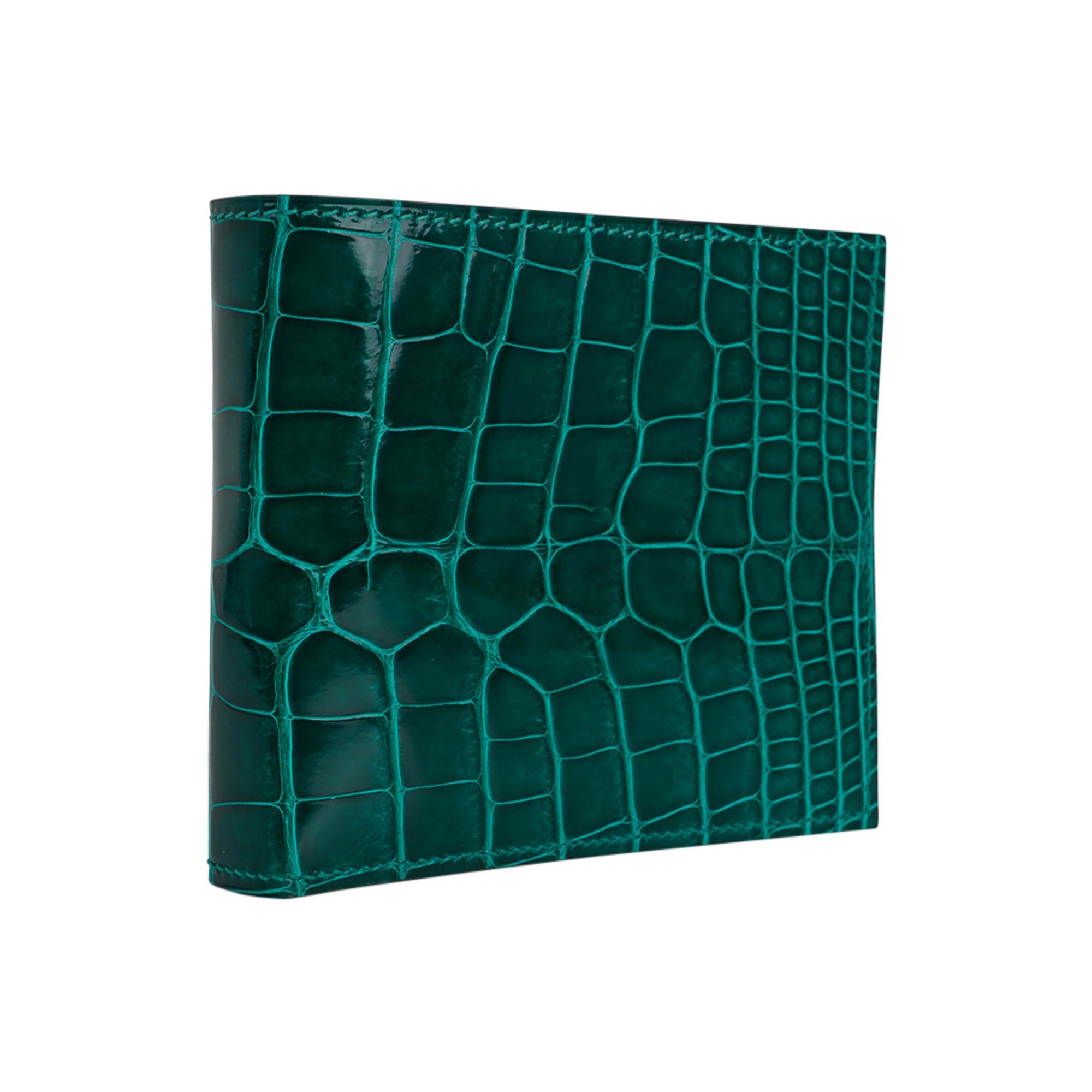 Mightychic offers a guaranteed authentic Hermes Men's MC2 Copernic compact bi-fold wallet featured in coveted jewel toned Emerald Alligator.
Interior is chevre with eight credit card slots, two flat pockets and one paper money slot.
Sleek clean