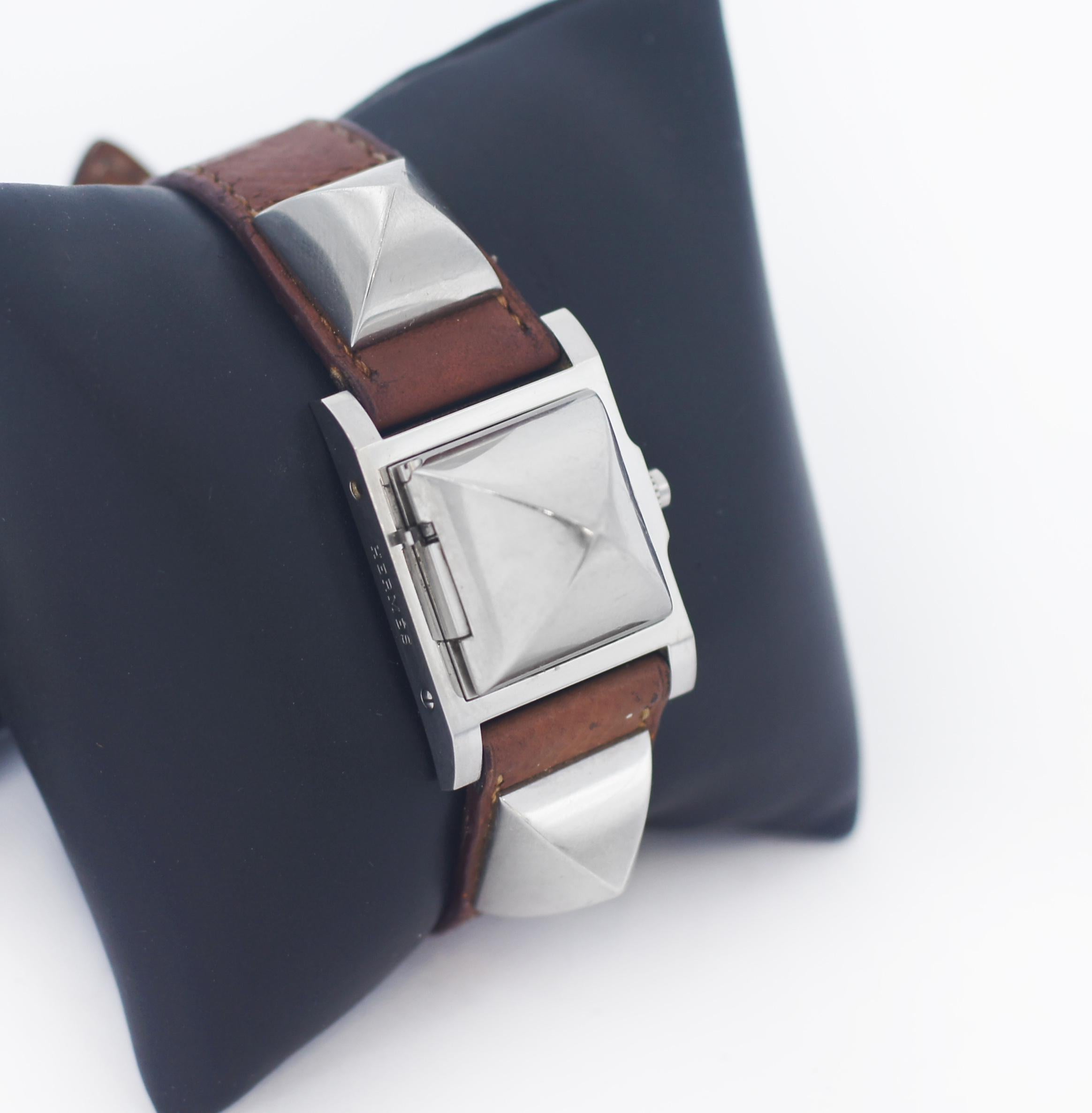 HERMES
Model num: ME2.210
Square: Case with cover
Production Approx. in 2010
Serial # on watch
Case: 23mm x 23mm
Band width: 18mm Hermes original band
Movements: Quartz
Color: Silver Studs, Brown Leather band
Material: Stainless steel
Country of