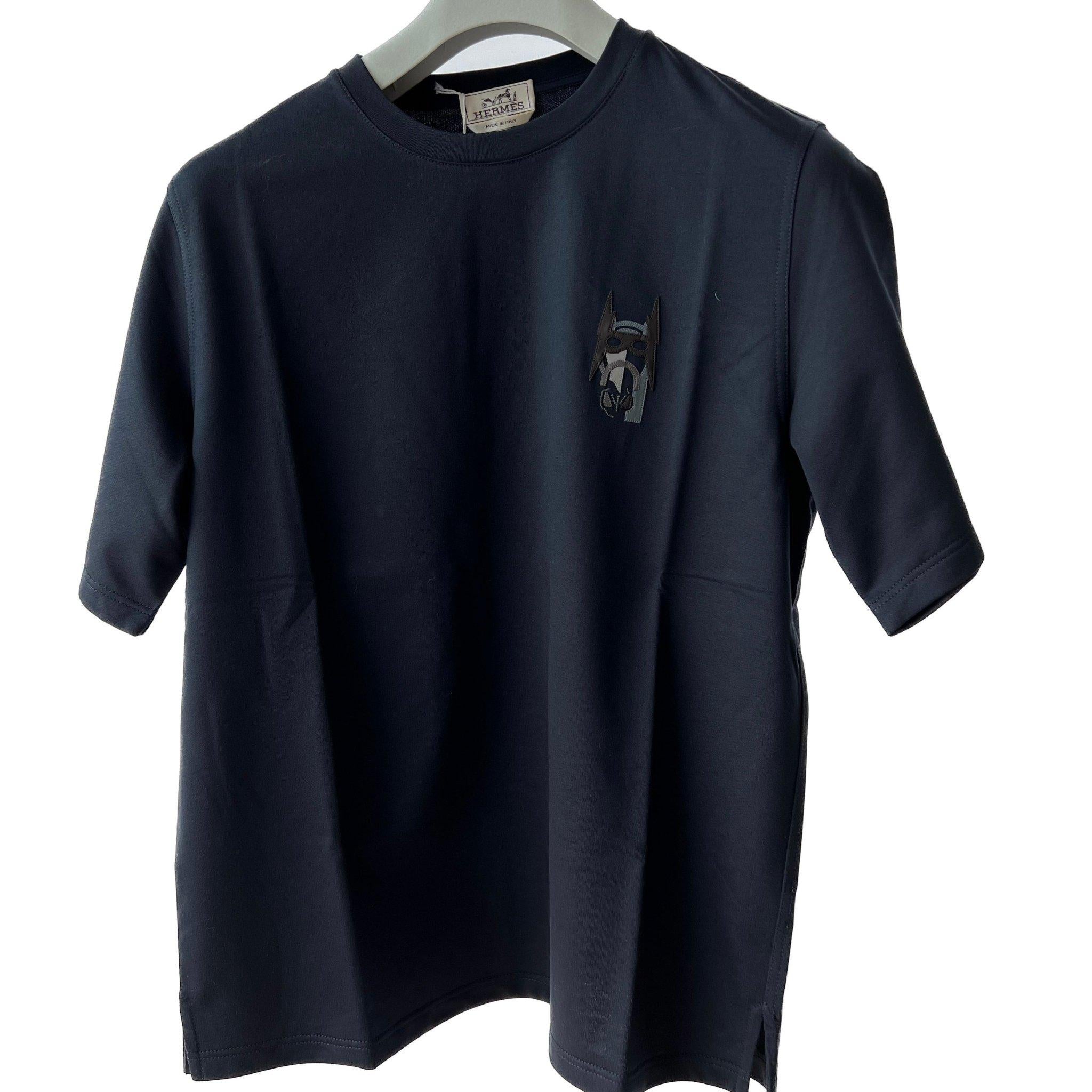The Hermes Mini Patch Cuir t-shirt is made from 100% cotton and comes in the blue shade Marine. It features the 'Super H' patch on the top right front. 

Brand: Hermès

Colour: Marine (Blue)

Material: 100% Cotton

Size: Medium

Condition: Unworn.