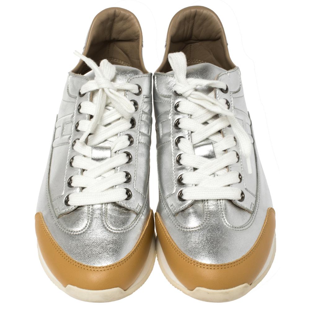 Let this pair of low-top Hermès sneakers elevate your style this season. Crafted from metallic silver and tan leather, these sneakers feature round toes and lace-ups on the vamps. They have been detailed with 'H' initials on the sides and made