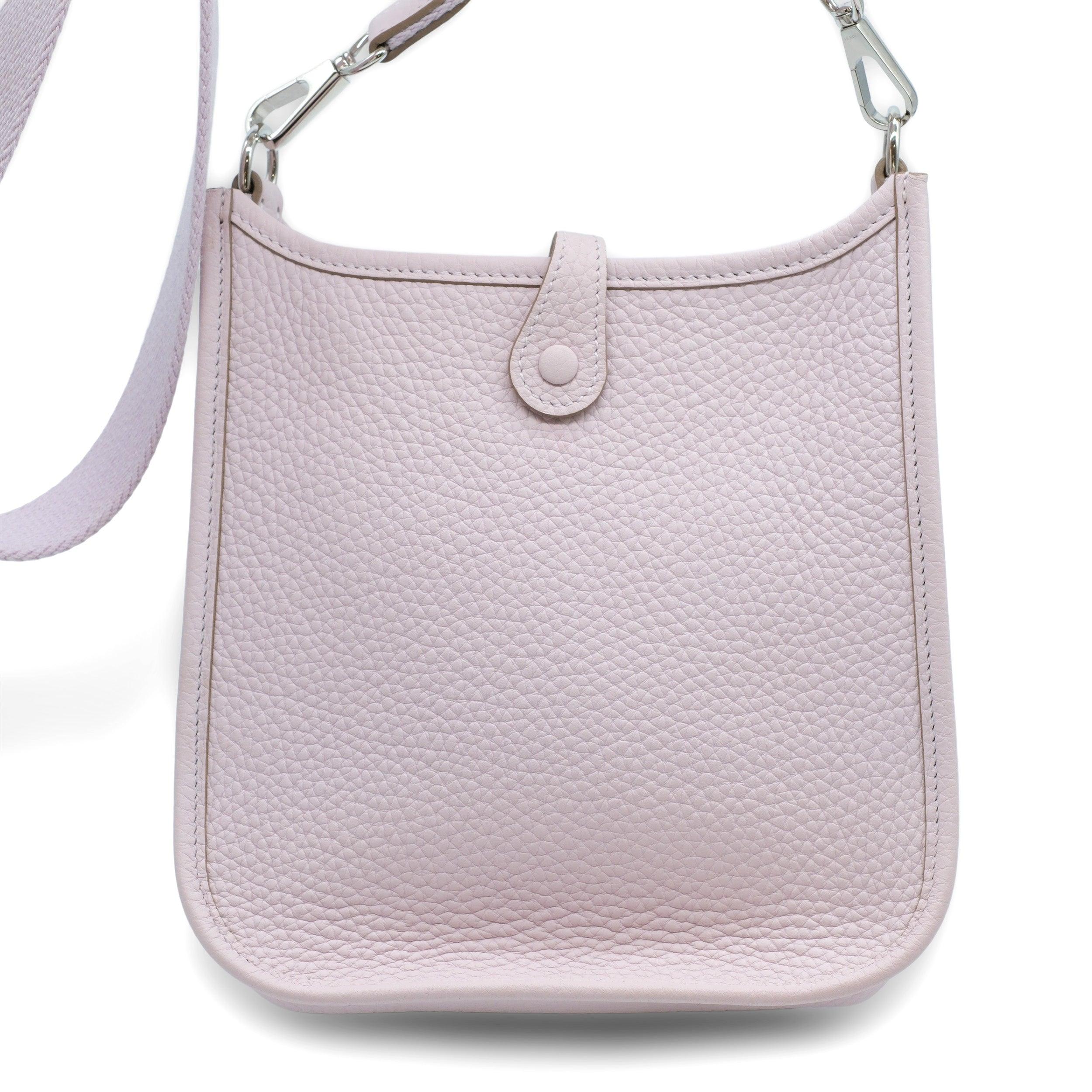 The Taurillon Clemence Evelyne TPM bag in Mauve Pale is an elegant small messenger bag made of Taurillon Clemence calfskin in pale pink. It features a perforated Hermes H oval on the front and a canvas shoulder strap with palladium hardware. The top