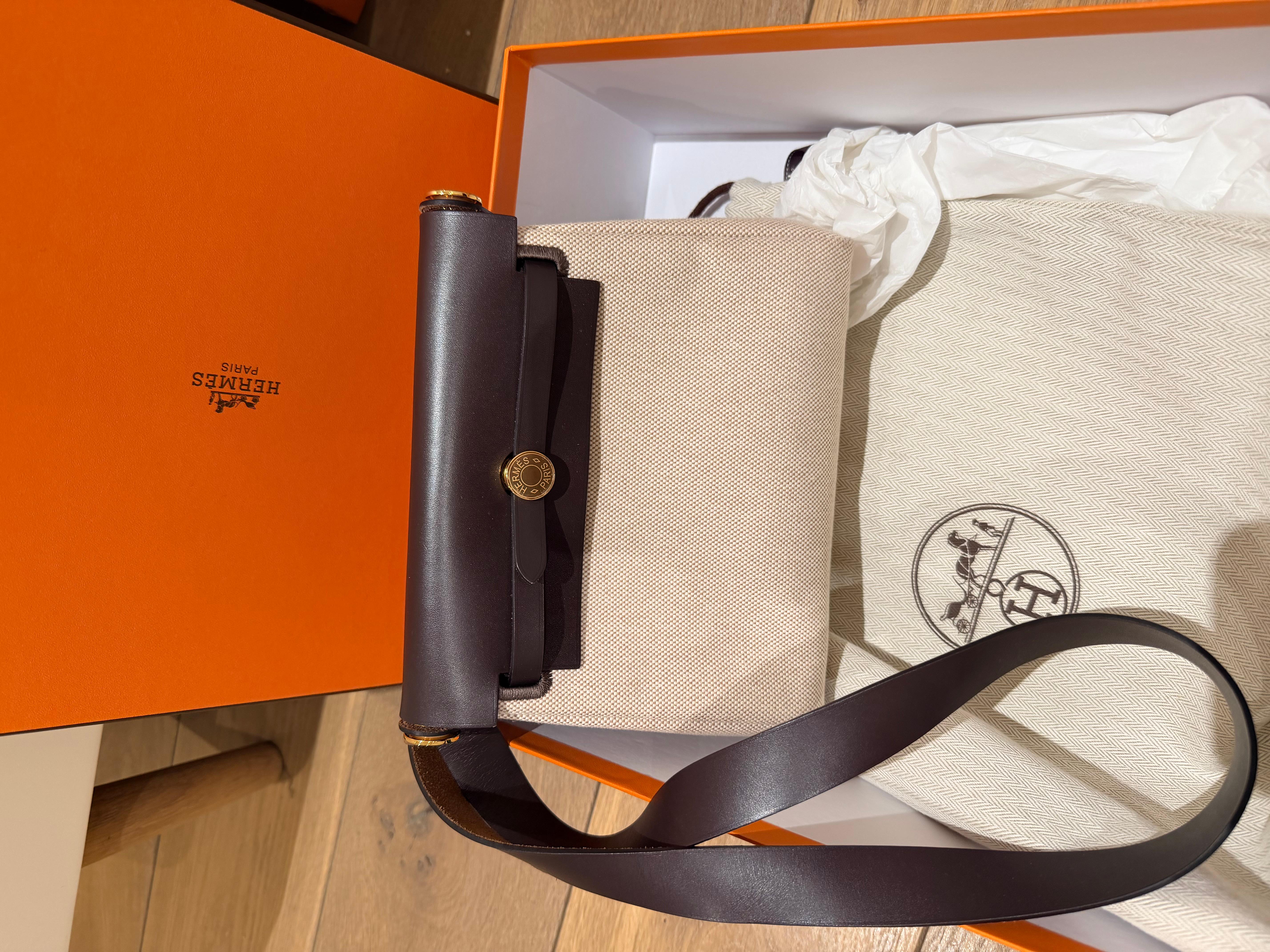 Borsa Hermes Mini Herbag 20 in Ecru Ebene.
Questa Hermes Herbag Mini combina la tela Ecru Beige Toile H con la pelle Ebene Vache Hunter, elegantemente accentuata dalla minuteria Hermes Herbag in oro. Dotata di una chiusura Clou de Selle, di un