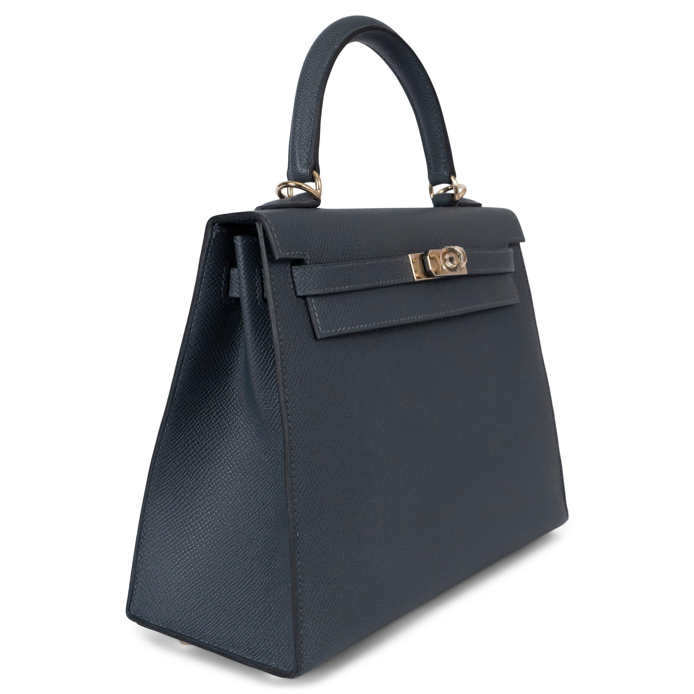 This 100% authentic Hermès Kelly 25 Sellier bag is crafted from Gris Misty (dark grey) Veau Epsom leather with rare permabrass hardware. The interior is lined in Chevre (goat skin) and features an open pocket against the front and a zipper pocket