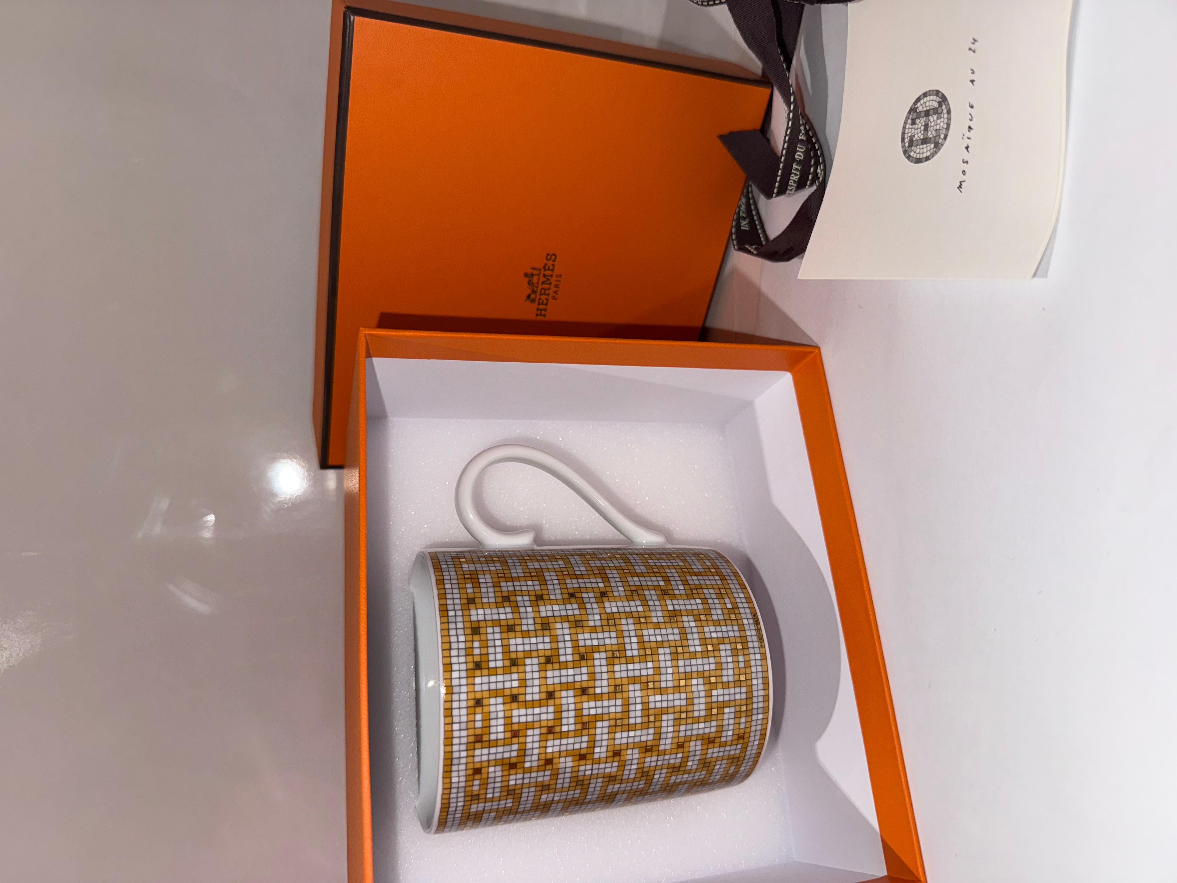 Hermes mug Mosaique au 24 gold, Mug in porcelain, Decorative mosaics are screen-printed and applied by hand using gold tiles. 

With its geometric pattern, the Mosaique au 24 gold collection reflects the original decor of the store at 24 Faubourg
