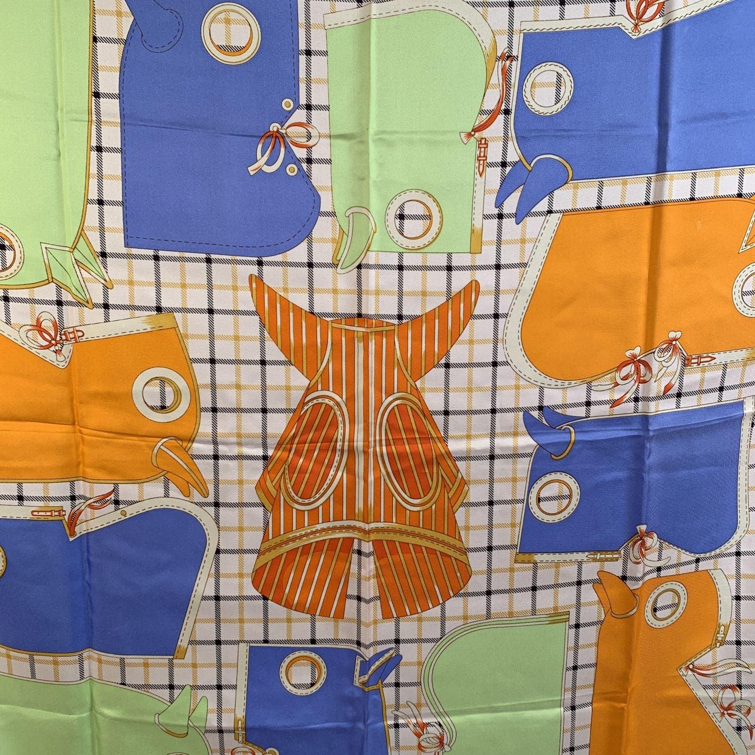 Beautiful Hermes 'Camails' silk scarf designed by Francoise de la Perriere and originally issued in 1974. The design depicts some horse hoods in light blue, orange and light green colors against a checkered white background. Hot pink border. Hand