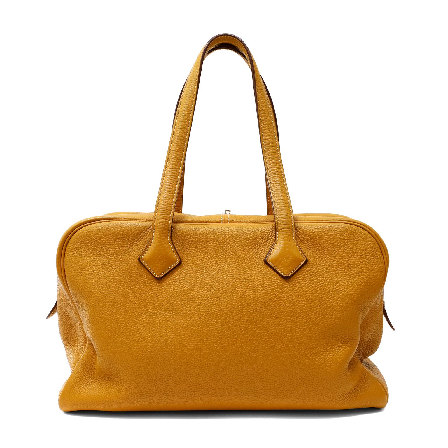 This authentic Hermès Mustard Clemence 35 cm Victoria II Bag is in excellent condition.  The relaxed silhouette is roomy and soft to the hand in textured mustard yellow Clemence leather.  Two-way double zip closure accesses the beige canvas