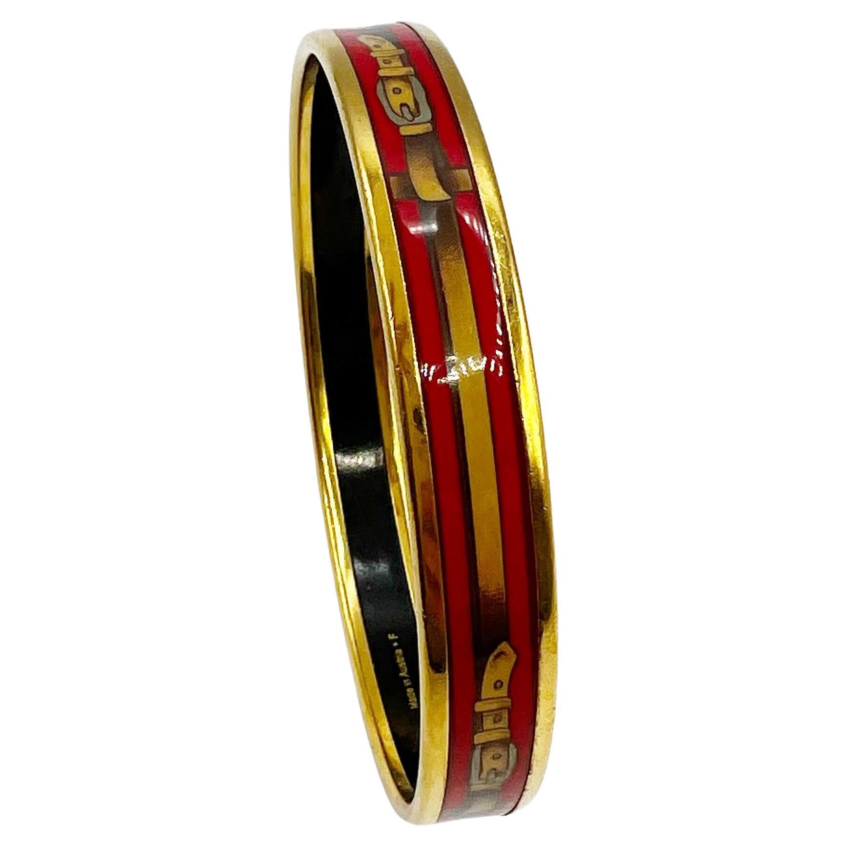 Questo braccialetto bangle stretto di Hermès, autentico al 100%, presenta un sorprendente disegno in smalto multicolore di una cintura in pelle, un'imbracatura, completata da una minuteria placcata in oro. Un mix perfetto di tonalità vivaci e