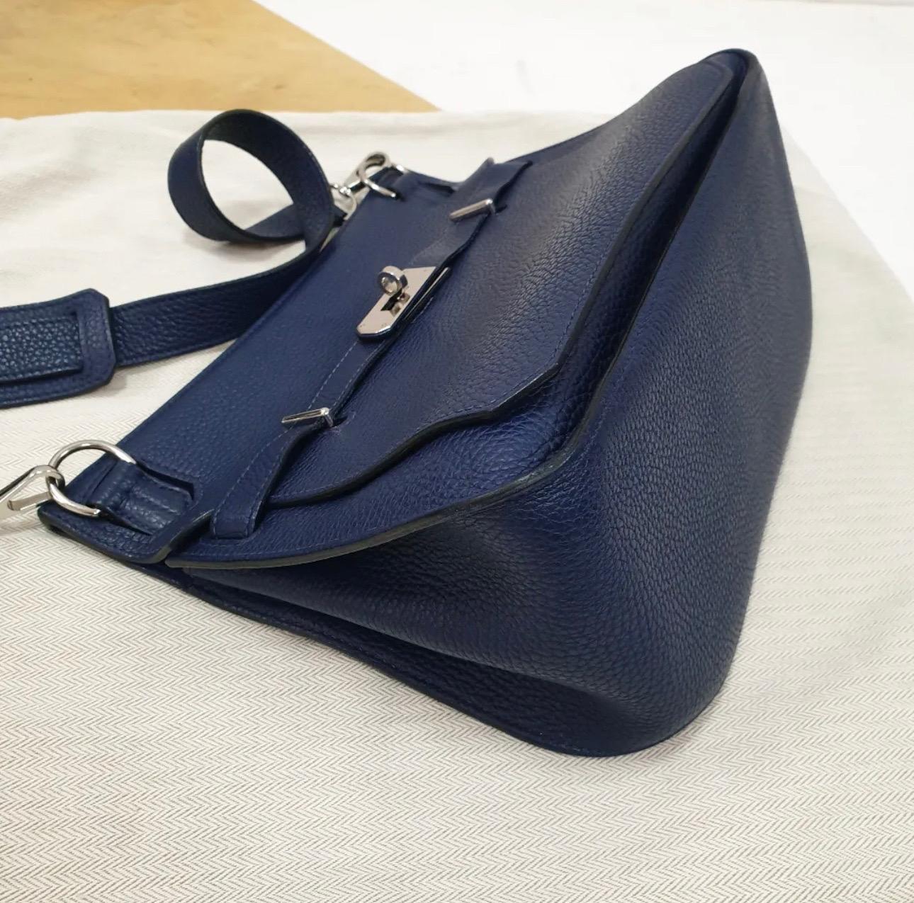 This authentic Hermès Navy Blue Clemence Jypsiere 28 is in pristine condition.  
With its Kellyesque design elements, the unisex Jypsiere is a much beloved messenger bag that may be worn cross body at varied lengths.  
Clemence is made from baby