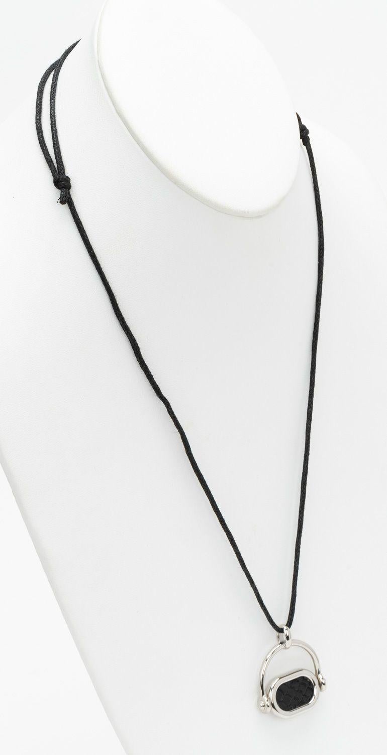 Collana Hermès in argento palladio con scritta Hermès su un lato, mentre sull'altro lato del ciondolo c'è una pelle di serpente nera. Le misure del ciondolo sono 1,25 x 1,5