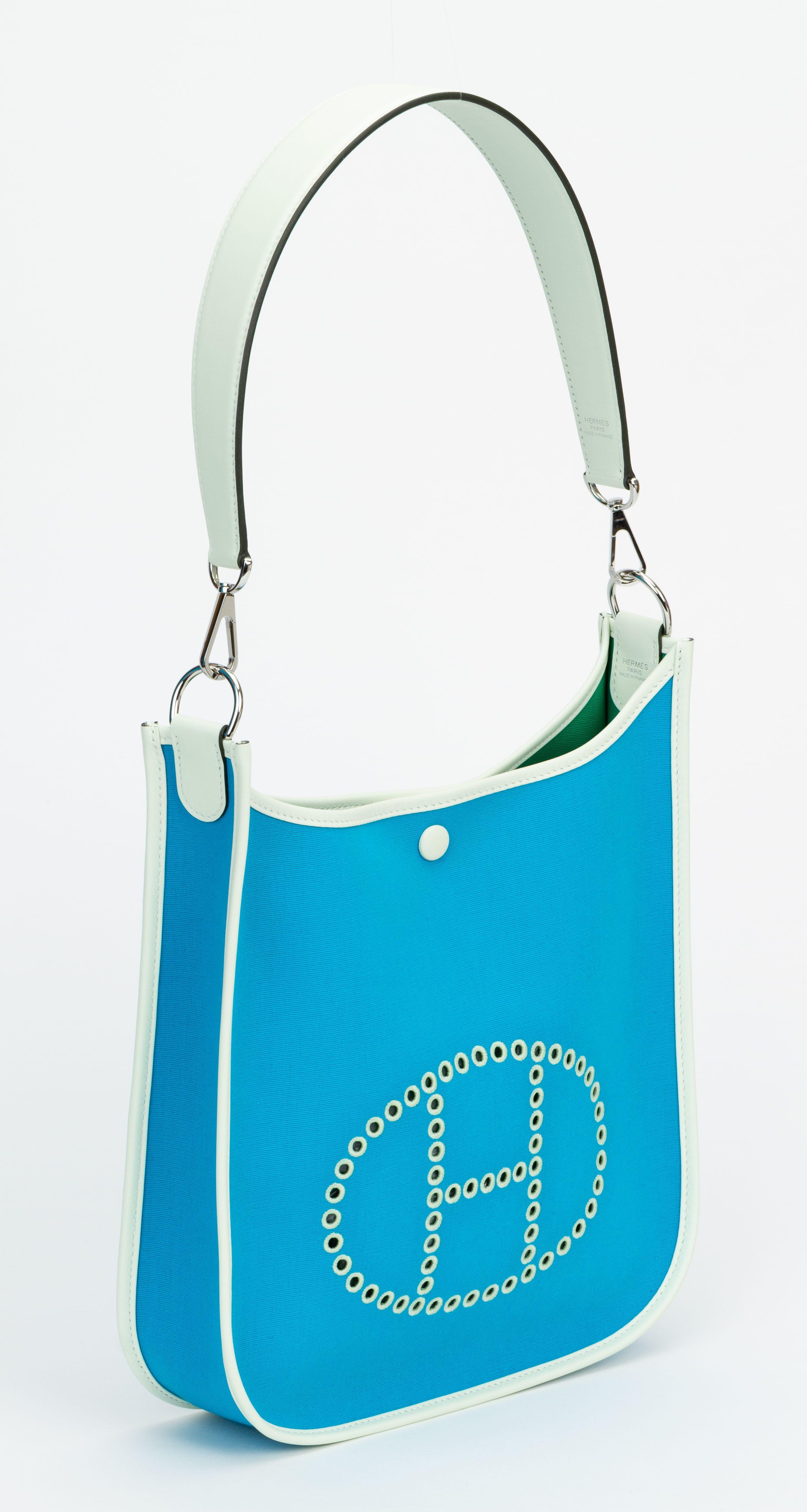 Questa Hermès Neo Evelyne PM è in tela Bleu Azteque Officier e pelle Vert Fizz swift con finiture in palladio, con cuciture tono su tono, grande H perforata in cerchio (davanti), chiusura a scatto con linguetta e tracolla in pelle rimovibile. Viene
