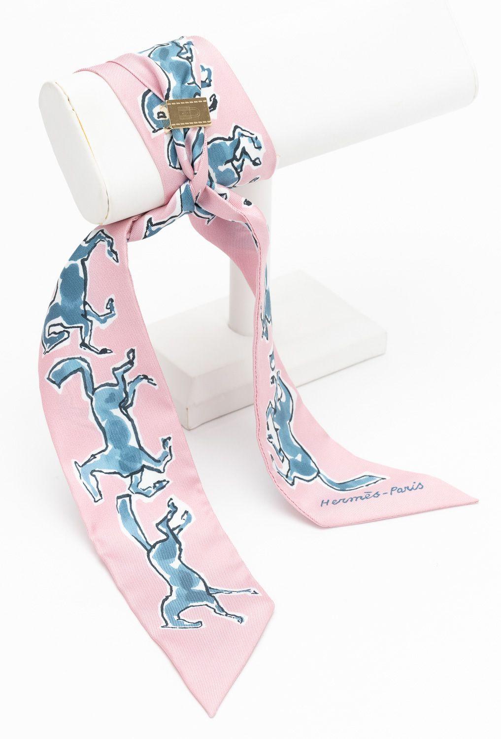 Hermès Horse Twilly in Rosé, with square slide. The pattern features horses in blue. The piece is in excellent condition. Comes with original box 