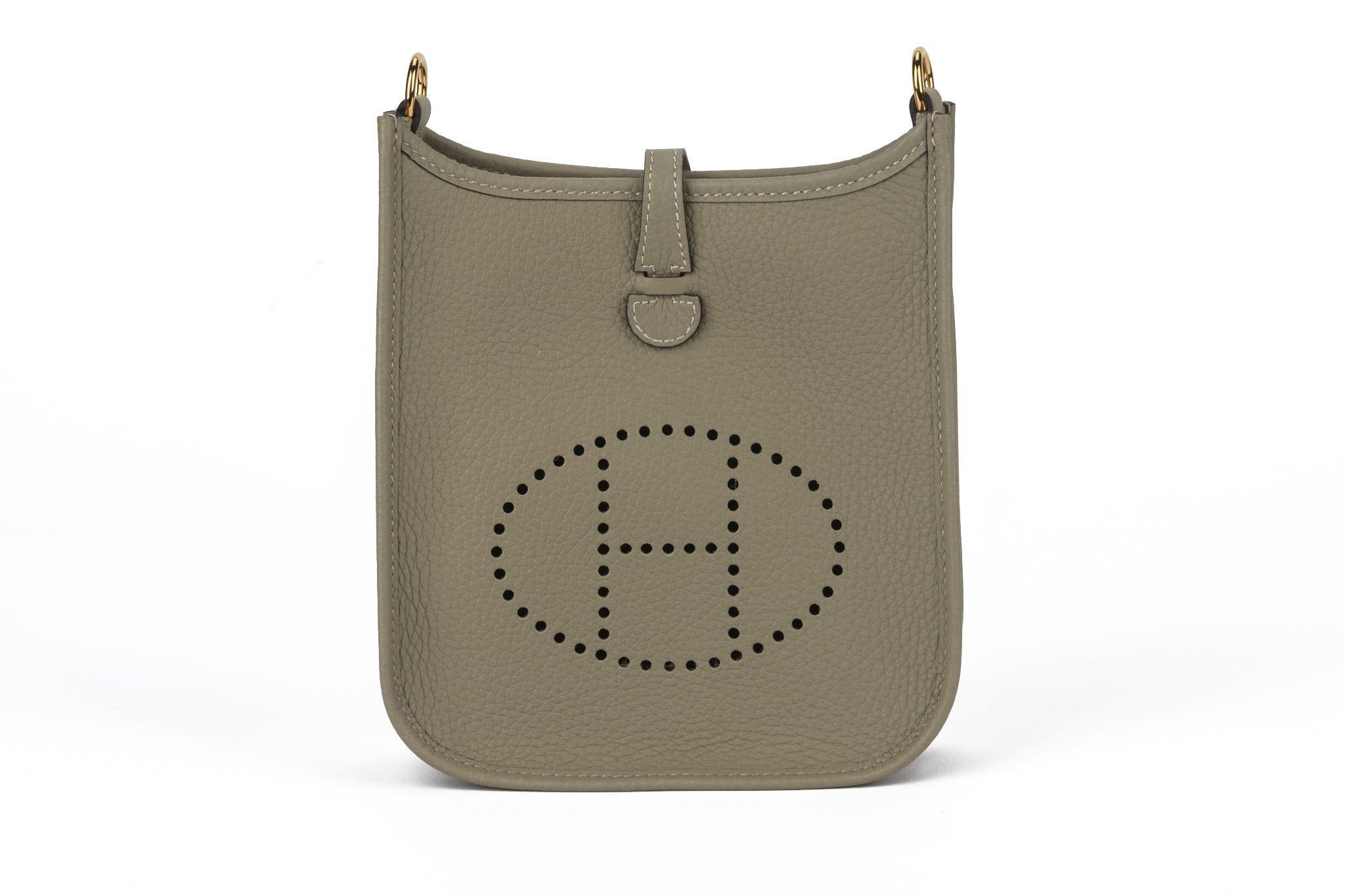 Hermes sage Evelyne TPM in clemence leather with canvas strap. Smallest model of Evelyne has tonal stitching, a large perforated H icon in circle at front, pull tab top closure, and a removable strap, 21