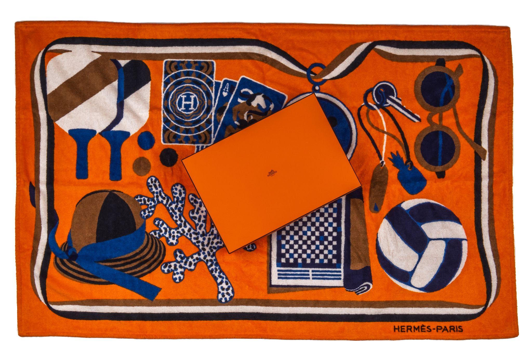 Hermès Beach Towel in orange. The pattern features the necessities for a beach day like a hat, headphones and sun glasses. The item is new and come in the box.