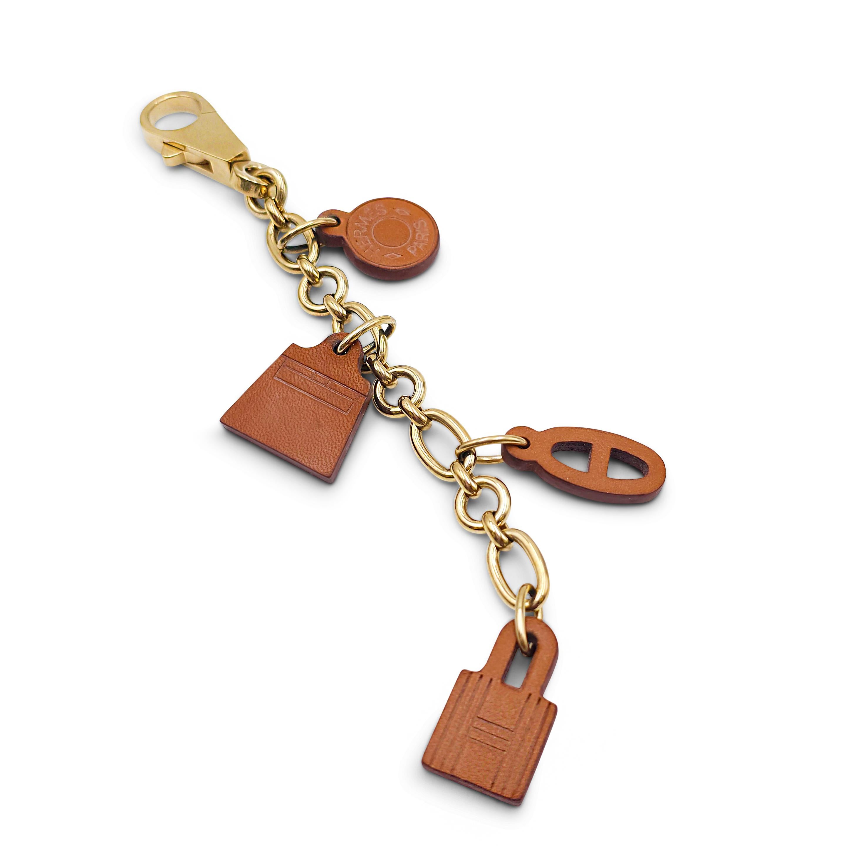 Authentic Hermès Olga bag charm featuring four of the brand's iconic charms crafted in Barenia leather.  The gold-tone chain measures 5 1/2 inches in length.  The cadenas lock charm hangs from the last link, bringing the total length of the bag