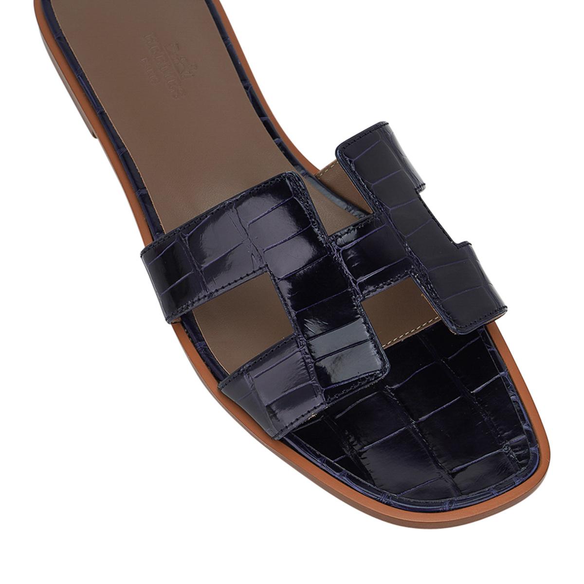 Mightychic offers a pair of Hermes Oran sandals featured in Bleu Marine Alligator.
This stunning limited edition Hermes Oran flat slide sandal is a neutral with a subtle punch of colour.
The iconic H cutout over the top of the foot.
Embossed
