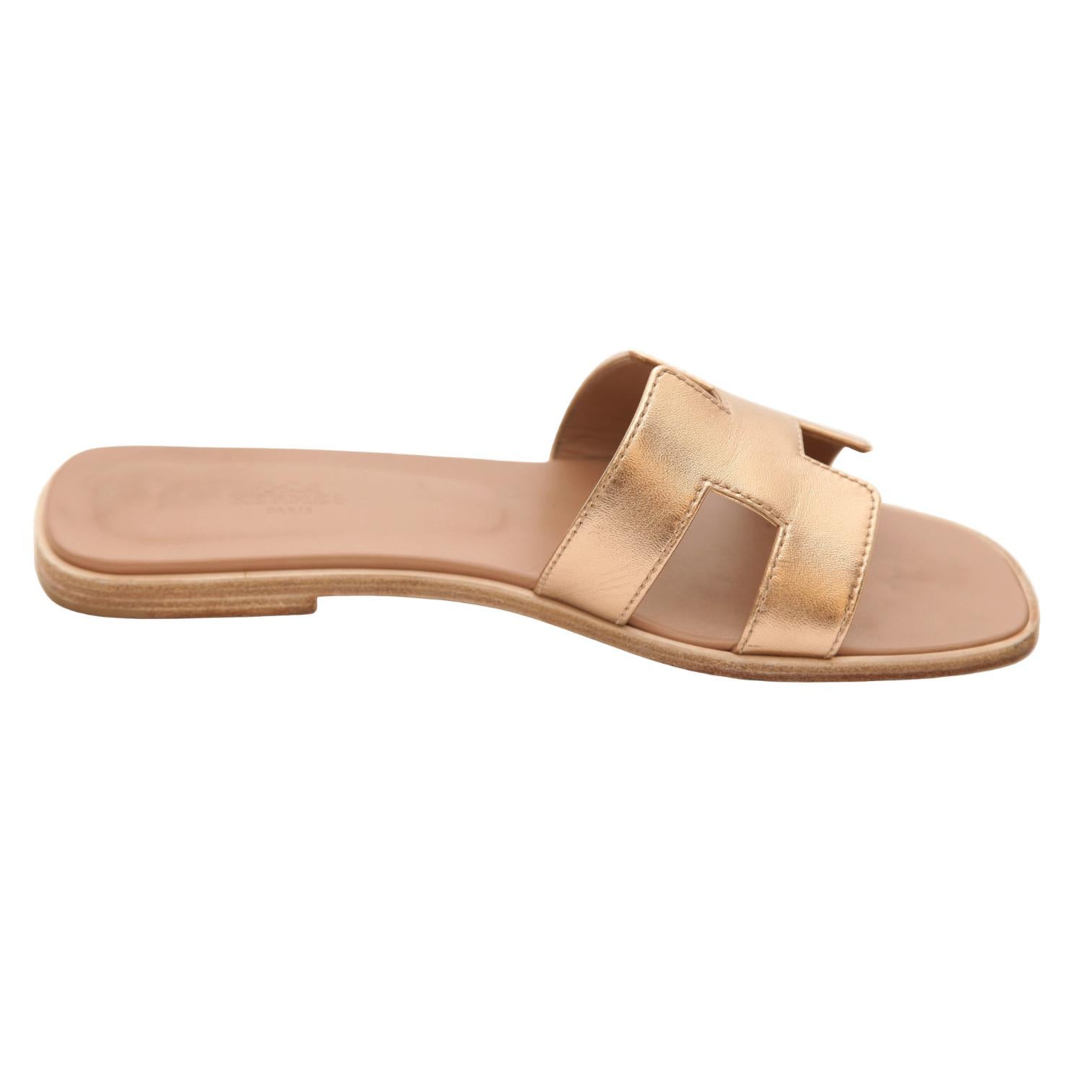 GUARANTEED AUTHENTIC HERMES METALLIC ROSE GOLD H ORAN SANDAL

Details:
- Metallic rose gold H Oran sandal.
- Comes with Hermes dust bags.

Size: 38

Measurements (Approximate):
- Insole, 9.75