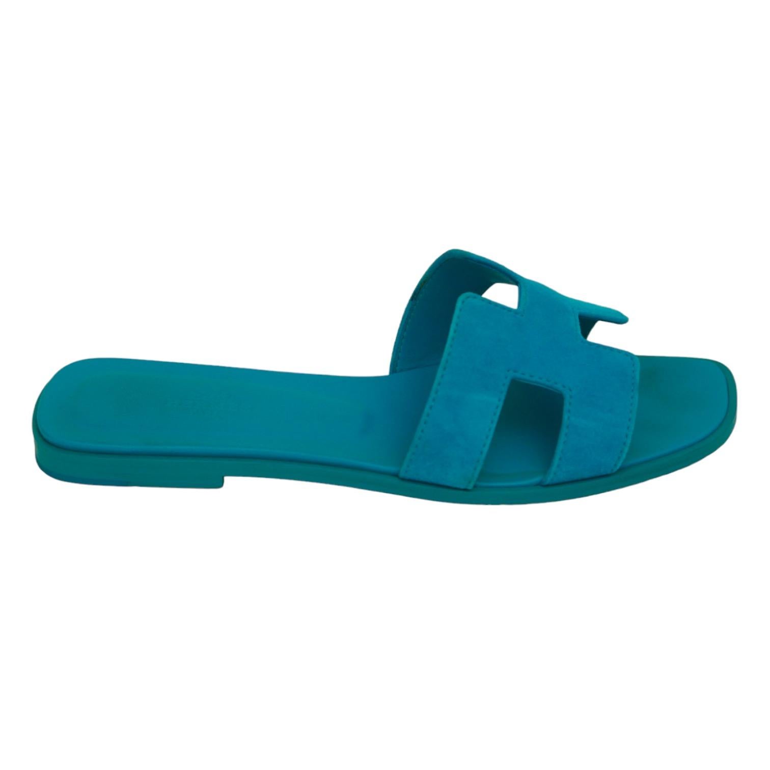 
GUARANTEED AUTHENTIC HERMES BLUE SUEDE ORAN SANDALS

Design:
- Blue suede uppers.
- Hermes H strap over vamp.
- Slip on.
- Leather insole and outsole.
- Comes with dust bag.

Size: 38

Measurements (Approximate):
- Insole: 9.5