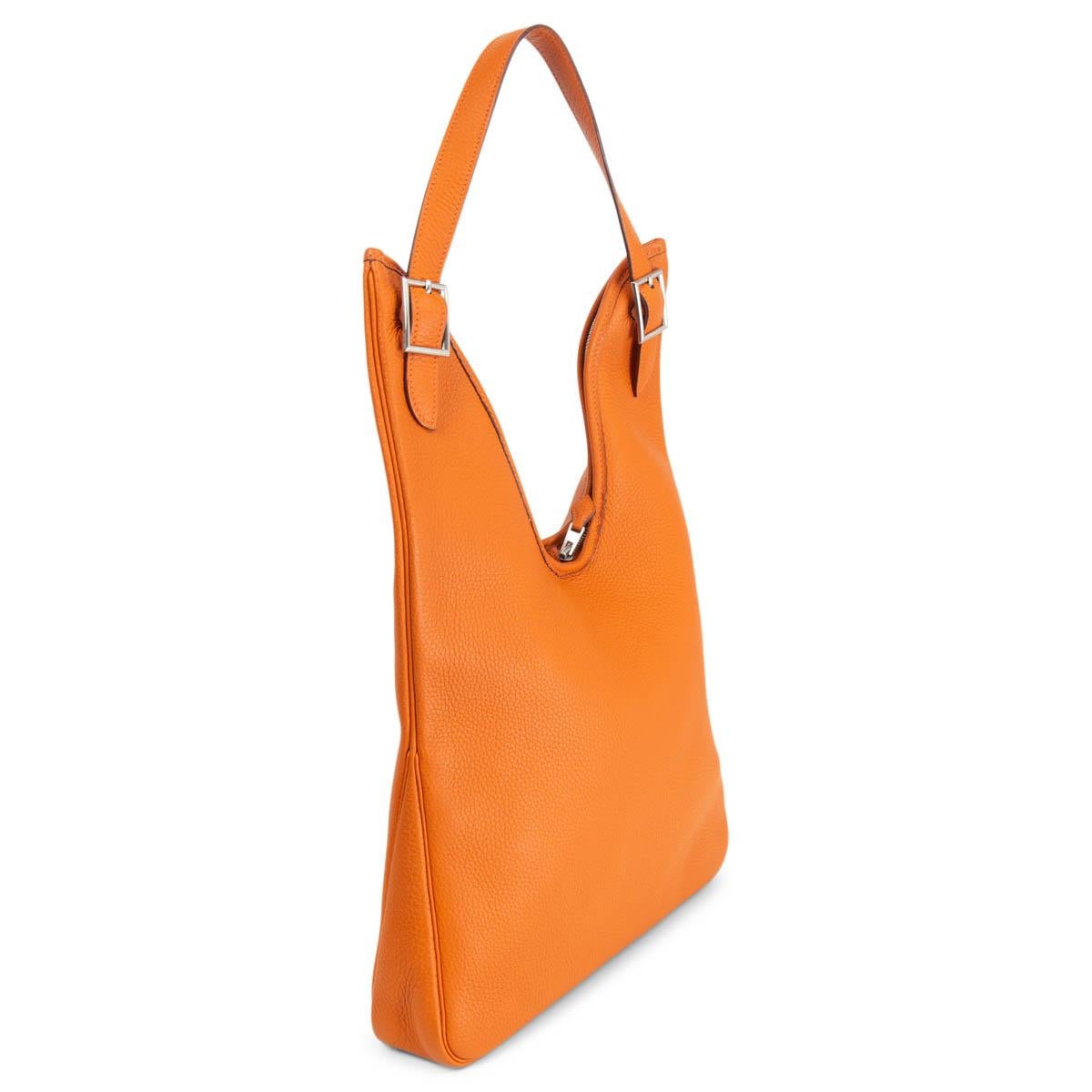100% authentic Hermès Massai PM hobo in orange Taurillon Clemence leather with Palladium hardware. Opens with a two-way zipper on top and is lined in classic off-white Hermès canvas with one zipper pocket against the back. Comes with a long and