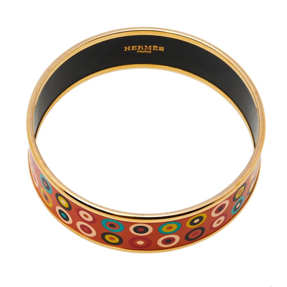 Grace your wrist with this stunner of a bracelet from Hermès. The piece has been crafted from gold-plated metal and decorated with orange enamel work on the surface featuring dancing circles. This bracelet is complete with the iconic label on the