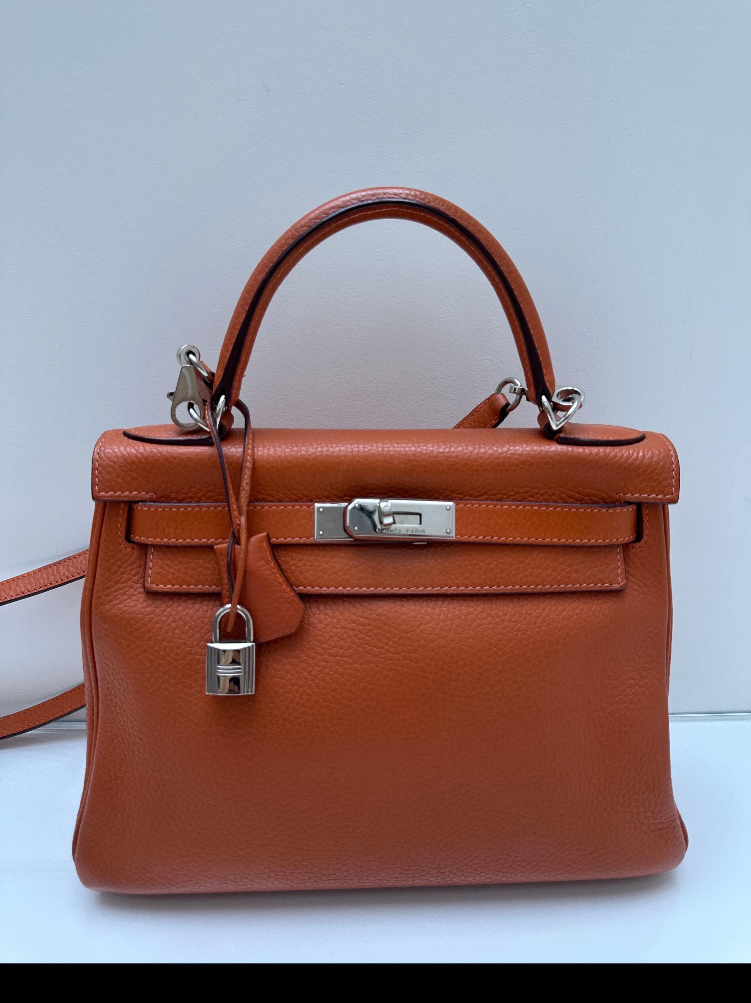 Borsa Kelly 28 arancione di Hermes. Classico colore arancione con hardware in palladio argento. Interni puliti. Buone condizioni. Rara taglia 25 Kelly. Include clochette, lucchetto, chiavi e sacchetto antipolvere. Garanzia di autenticità. 