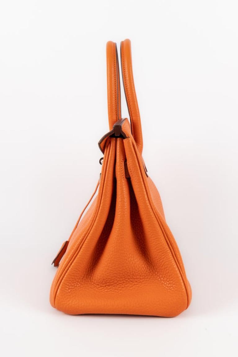 Hermès - (Made in France) 30 cm lange Birkin-Tasche aus orangefarbenem Clemence-Jungstierleder mit palladiertem, silbernem Metallverschluss und Gliedern, mit doppeltem Henkel, Schlüsseln unter einer kleinen Cloche und einem Vorhängeschloss.