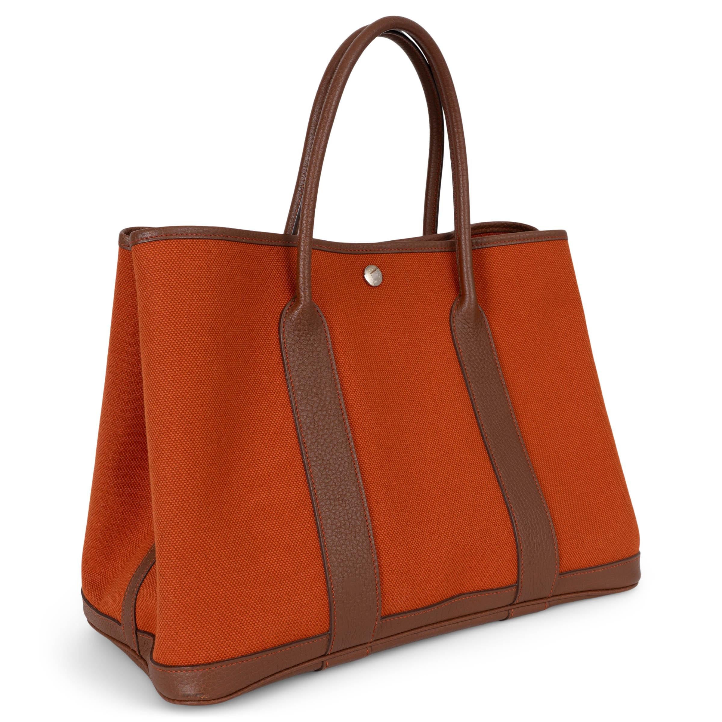 Ce fourre-tout Garden Party 36 100 % authentique est réalisé en toile Toile Militaire orange vibrante, avec des bordures en cuir Marron d'Inde Veau Negonda marron et des surpiqûres orange. Il est doté de deux poignées tubulaires et se ferme à l'aide
