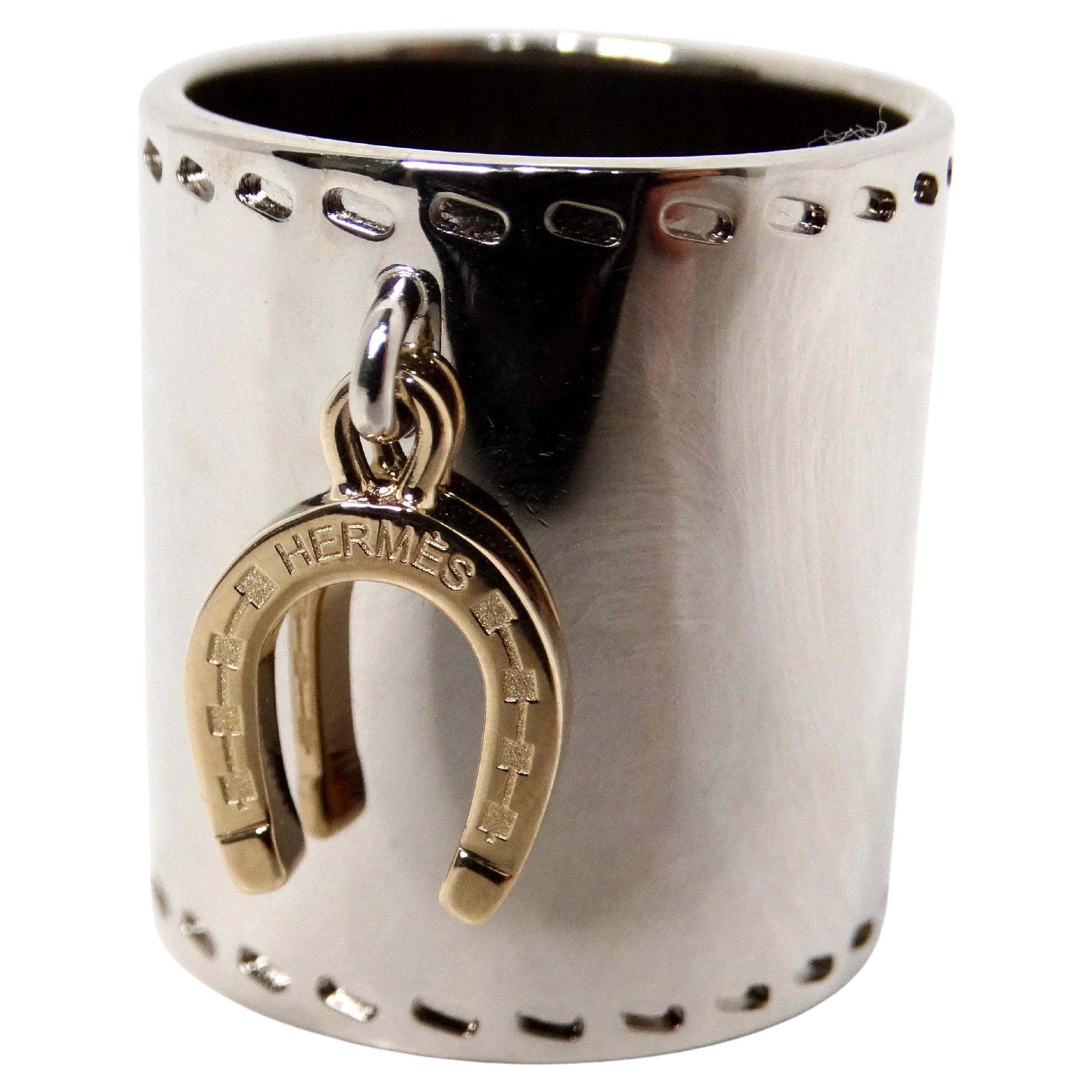 The Hermès Palladium Horseshoe Charm Scarf Ring embodies the perfect blend of luxury and whimsy, making it an exquisite addition to any accessory collection. The ring features a striking silver-tone base, beautifully complemented by a gold-tone