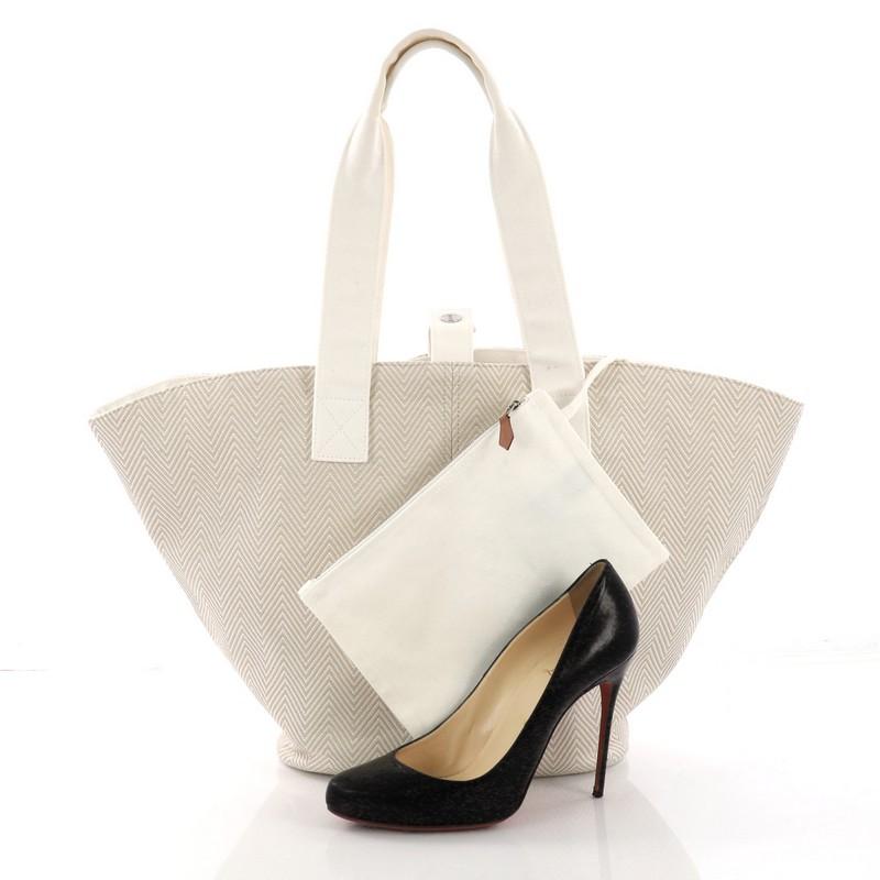 This Hermes Panier De Plage Handbag Canvas PM, crafted in beige ecru toile canvas, features dual flat handles and palladium-tone hardware. Its wide open top showcases a white canvas interior. **Note: Shoe photographed is used as a sizing reference,