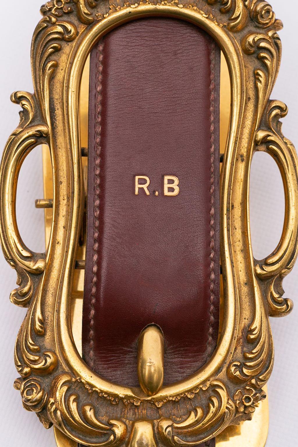 Hermes -Papiergewicht aus Leder und Goldplatte, die eine Gürtelschnalle darstellt - persönlicher Gegenstand mit Datum und Initialen R.B.

Zusätzliche Informationen: 
Abmessungen: Länge: 21,5 cm (8,46