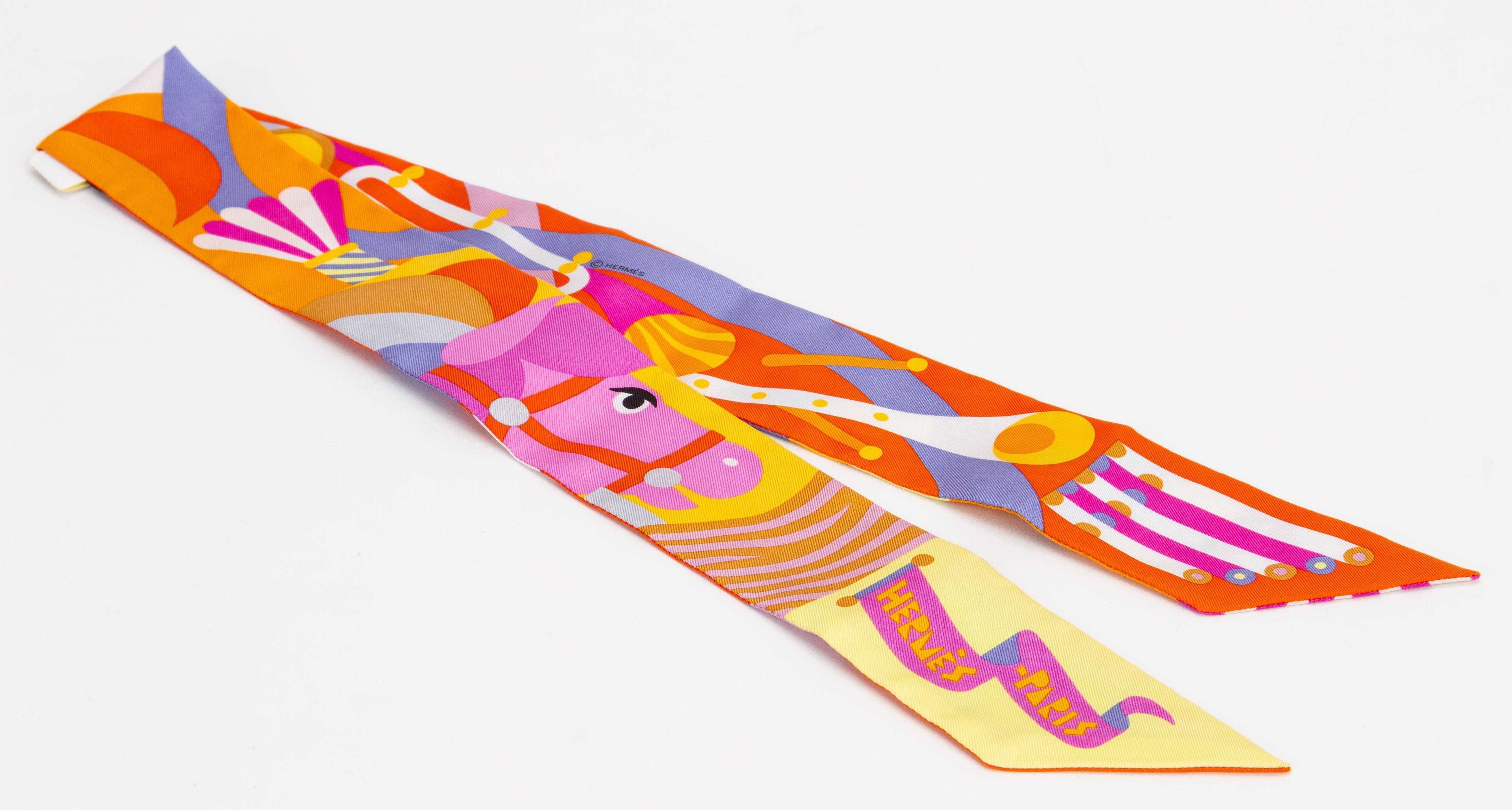 Sciarpa Hermès Silk Twilly di colore arancione con un divertente e vivace motivo Parade en Fanfare. Viene fornito con scatola originale e mendor argentato.