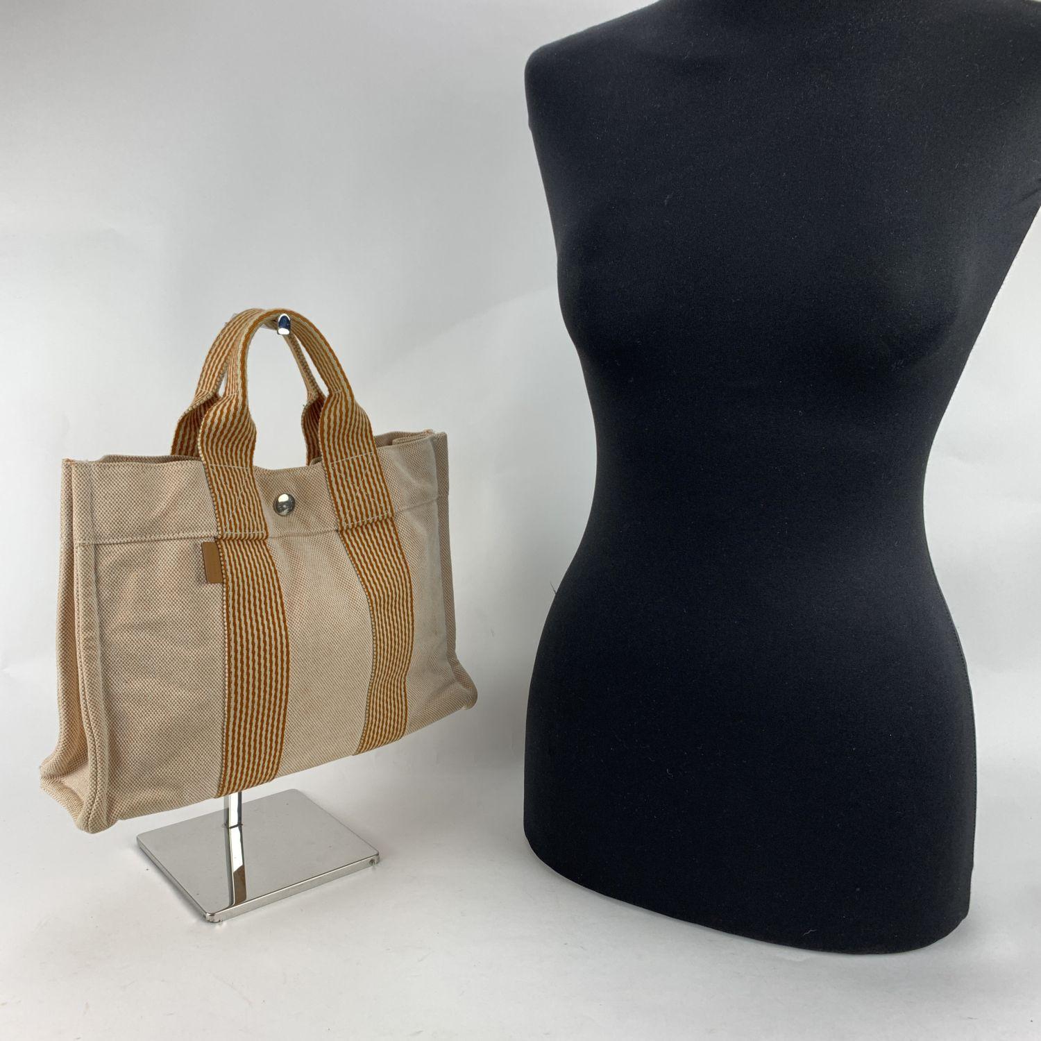 Model: 'HERMES FOURRE TOUT - PM' Tote handbag. Made in France. Beige canvas and orange stripes. Material: 100% cotton. It has snaps on both ends for expansion. Durable canvas handles, perfect for casual and everyday use. Open top with middle snap
