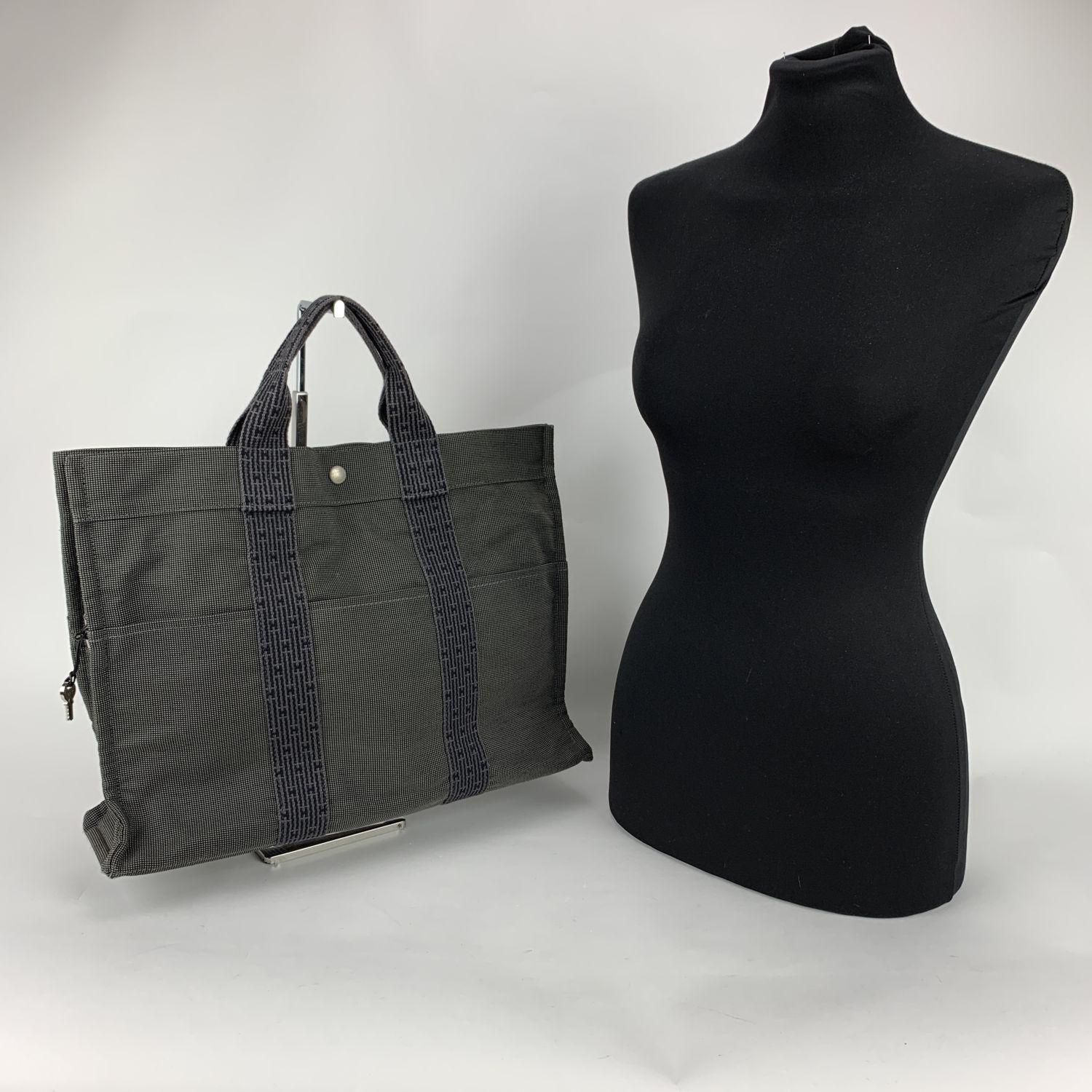 Hermes Canvas Herline Her Line MM Tote Bag in grey color. Made of a durable canvas. The tote has durable strap handles of a patterned Hermes H canvas. 3 open pockets on the front. Composition; 69% Polyamide, 31% Polyester. 3 snap button closure +