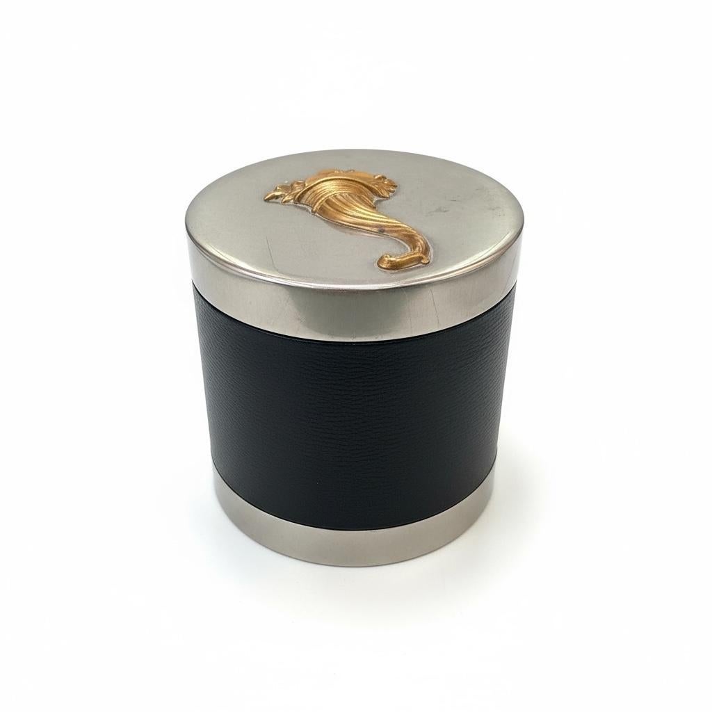 A symbol of abundance, rendered with restraint.

Crafted in 1970, this modernist Hermès charm box embodies the refined material contrasts and clean geometry characteristic of the era. Clad in smooth black leather and trimmed in silver plate, the