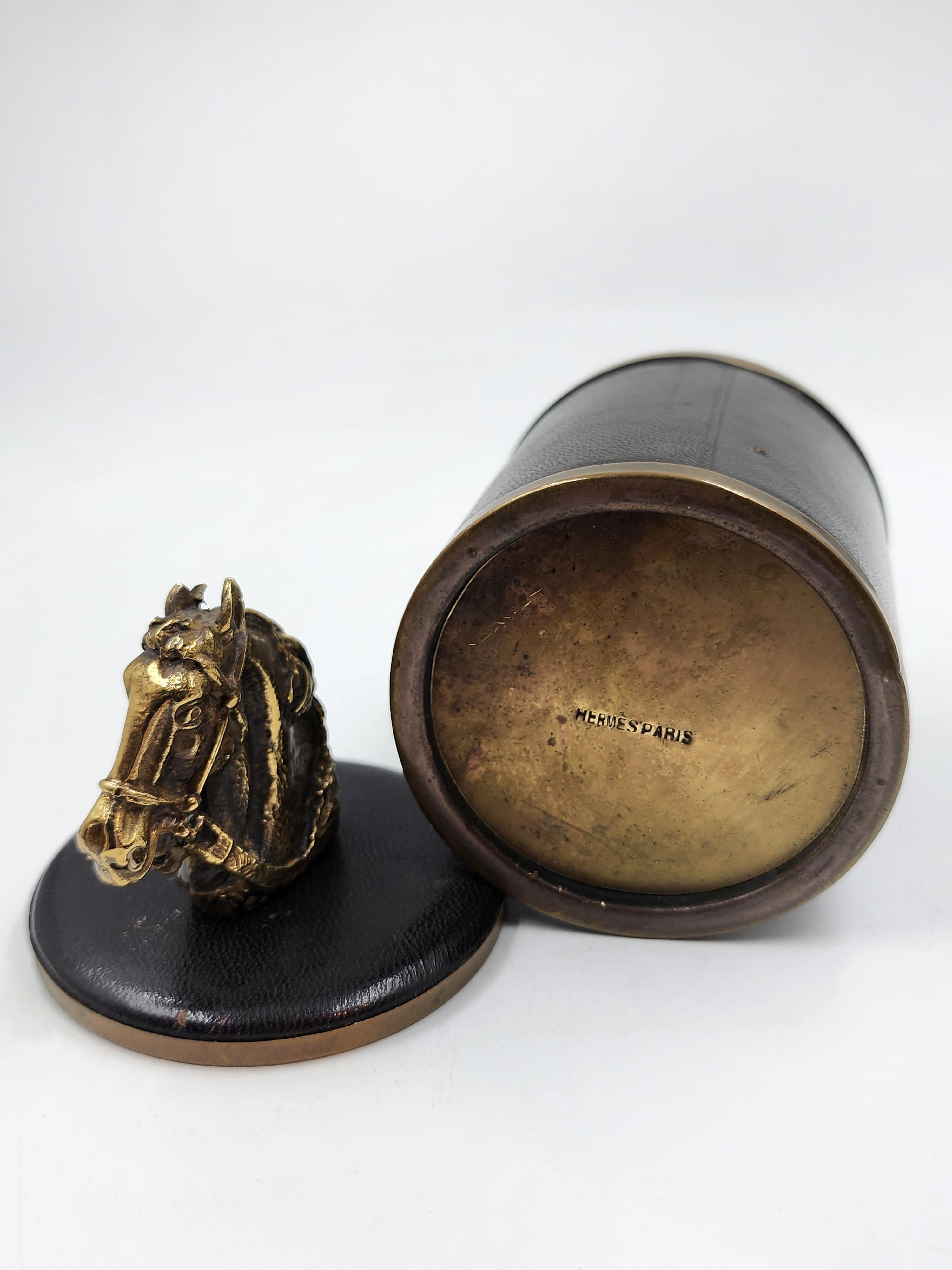Hermès Paris decorative box in leather and bronze.
This Hermès Paris decorative box features a cylindrical design covered in textured black leather on the exterior. The top and bottom edges are accented with bronze bands, and the base is also