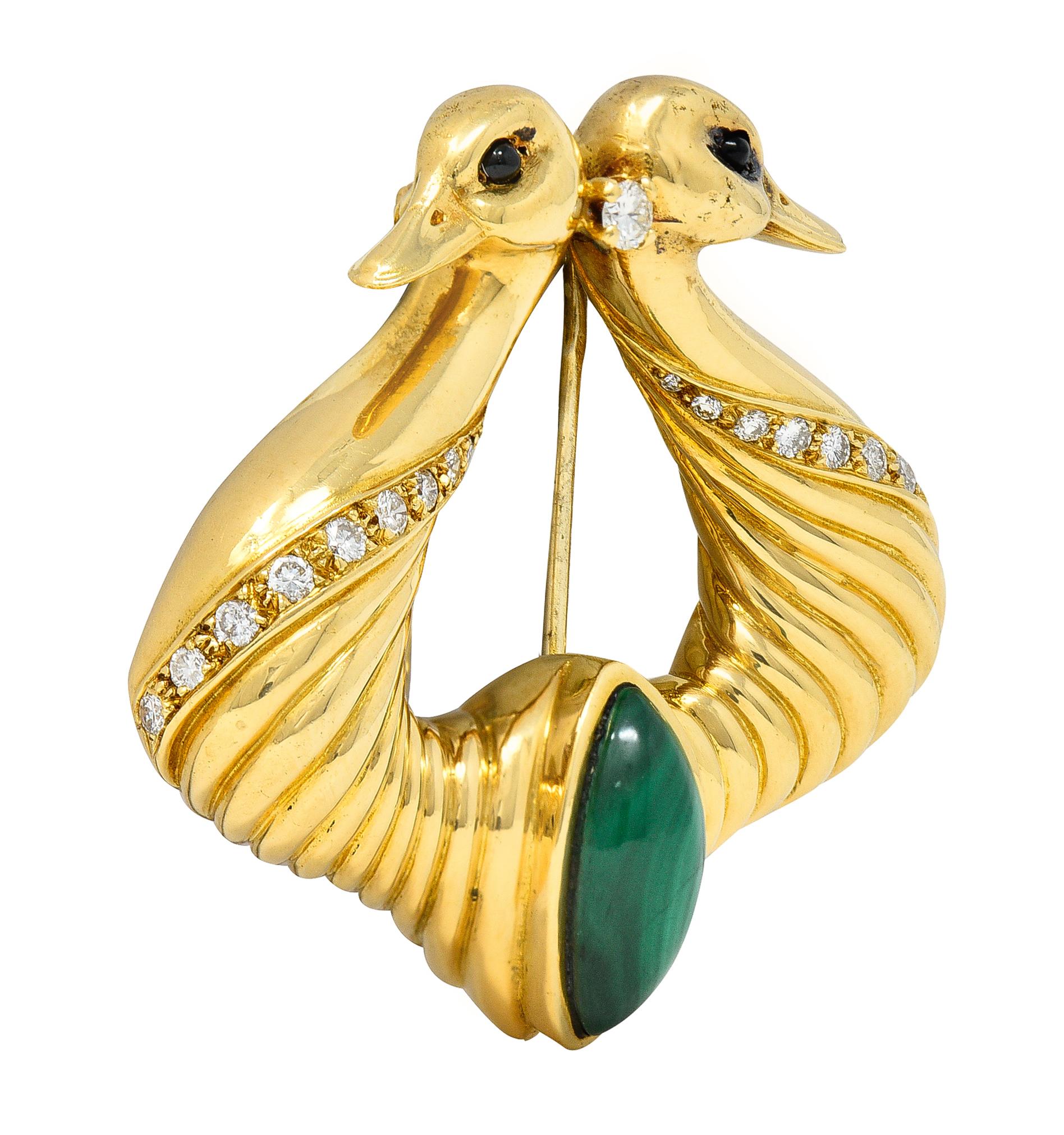 Designed as two stylized swans back-to-back with fluted bodies 
Centering a bezel set navette shape malachite cabochon 
Measuring 7.0 x 15.0 mm - banded light to dark green 
Featuring a round brilliant cut diamond prong set between heads
With