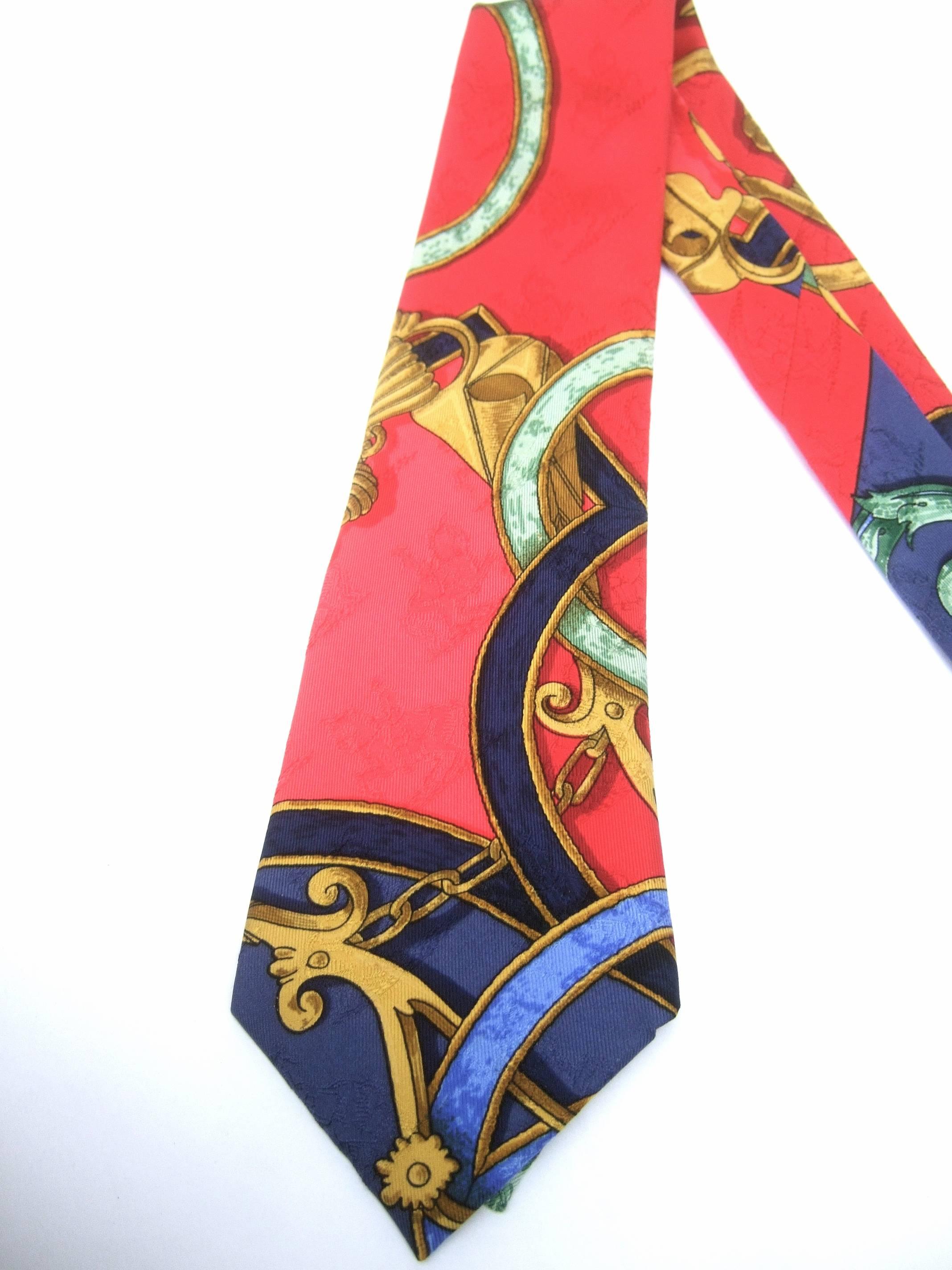 Hermes Paris Elegant graphic print silk necktie c 1990s
The stylish silk necktie is illustrated with golden buckles 
and gilt style chains that are illuminated against 
a crimson red two-tone background

Riding horseman are subtly visible in
