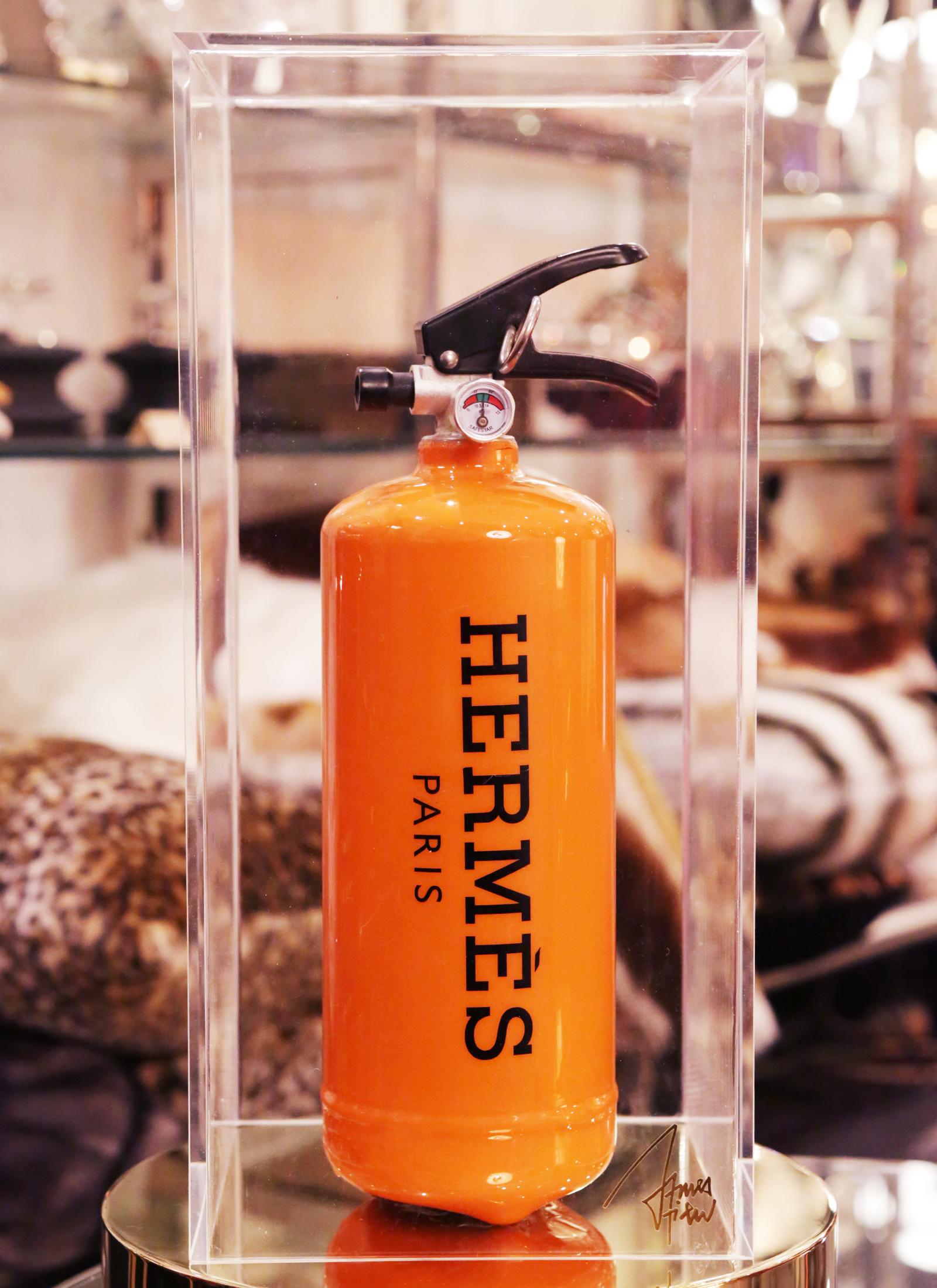 Feuerlöscher Hermes Paris. 
Limitierte Auflage von 25 Stück. Außergewöhnliches Stück. 
Unter Plexiglasbox. 
Maße: Schachtel: L 20 x T 20 x H 42::5 cm. 
Feuerlöscher: L 10::5 x T 10::5 x H 35::5 cm.