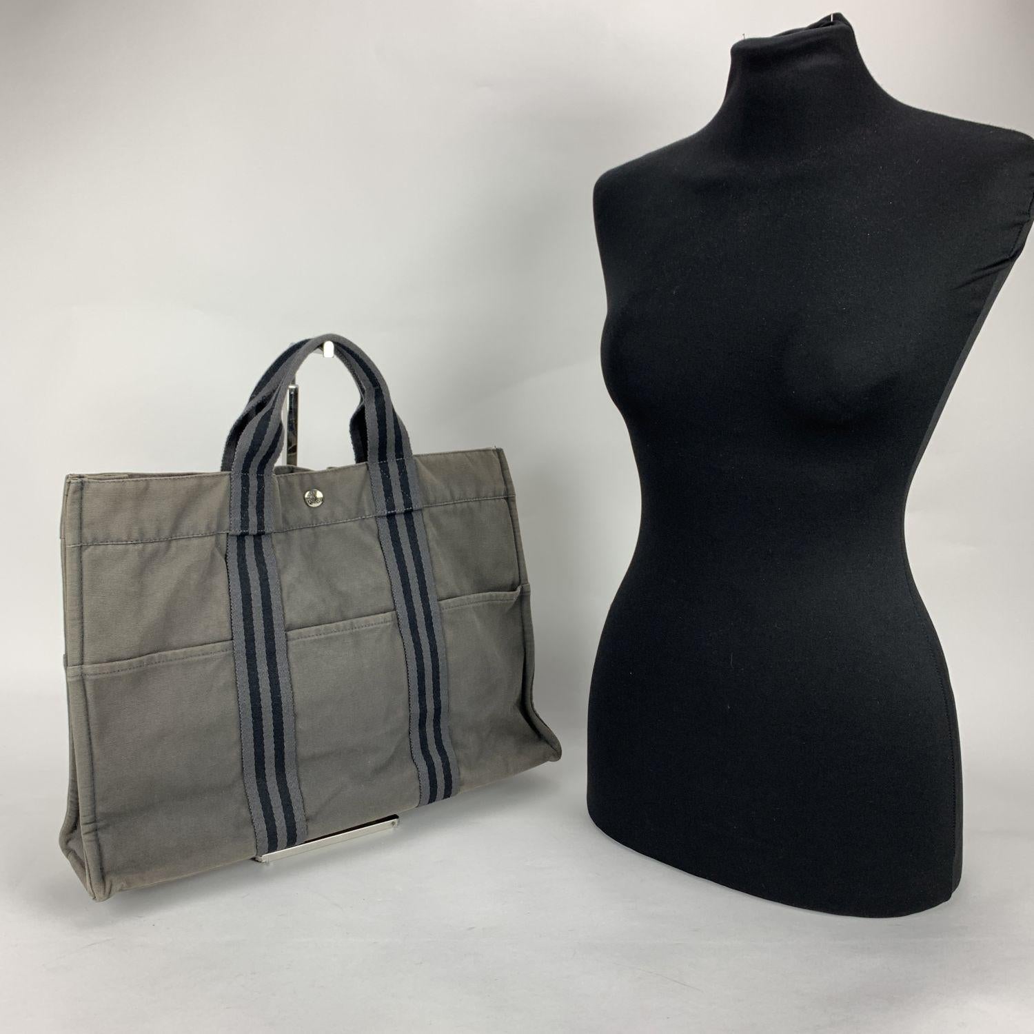 'HERMES FOURRE TOUT - MM' - Tote handbag. Made in France. Grey color with black stripes. Material: 100% cotton. It has snaps on both ends for expansion. Durable canvas handles, perfect for casual and everyday use. 3 open pockets on the front and 3