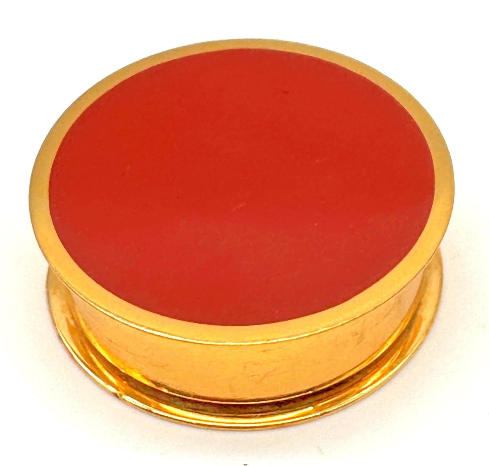 Hermès Paris Ormolu und Karneol Emaille Pillendose / Schmuckdose, Made in France, ca. 1960-1980er Jahre

Eine schicke und fein gearbeitete runde Dose von Hermès Paris aus Ormolu mit einem auffälligen Deckel aus karneolroter Emaille, hergestellt in