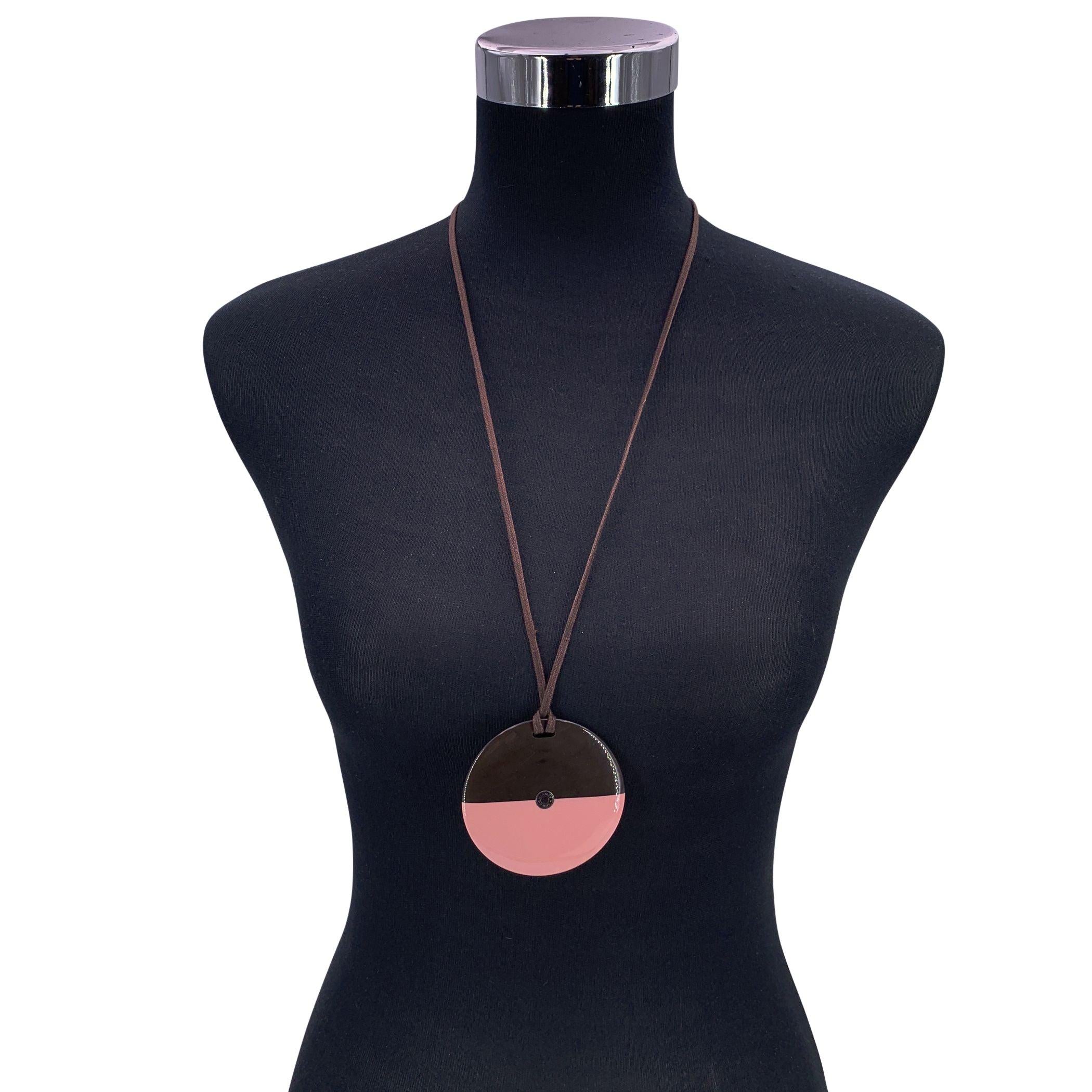 La collana rotonda di Hermès è uno splendido esempio di eleganza naturale e di artigianato contemporaneo. Il design bicolore in marrone e rosa tenue crea un contrasto raffinato e moderno. Sospeso da un cordoncino regolabile in cotone cerato,