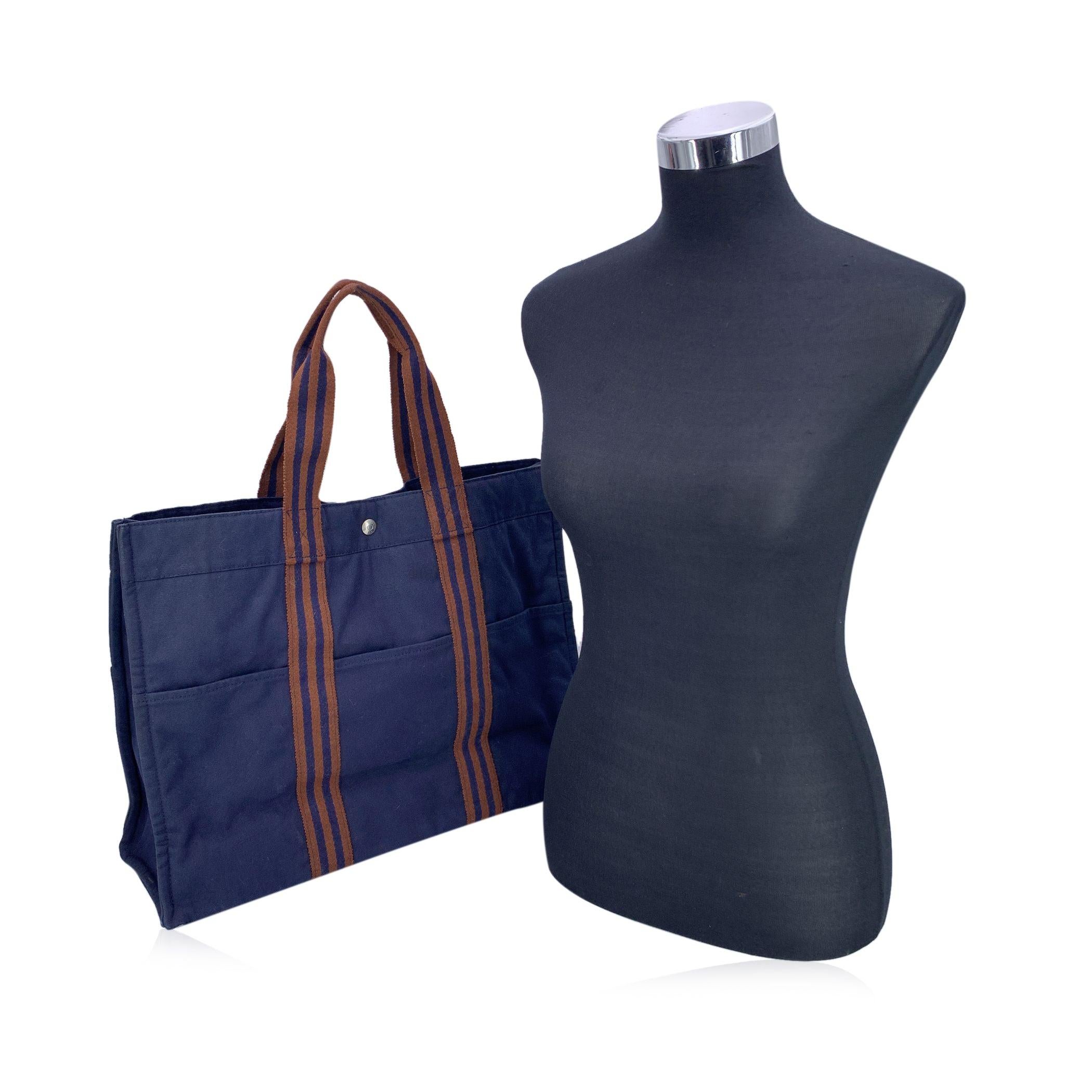 HERMES FOURRE TOUT - MM' - Tote handbag. Made in France. Navy Blue color with brown stripes. Material: 100% cotton. It has snaps on both ends for expansion. Durable canvas handles, perfect for casual and everyday use. 3 open pockets on the front and