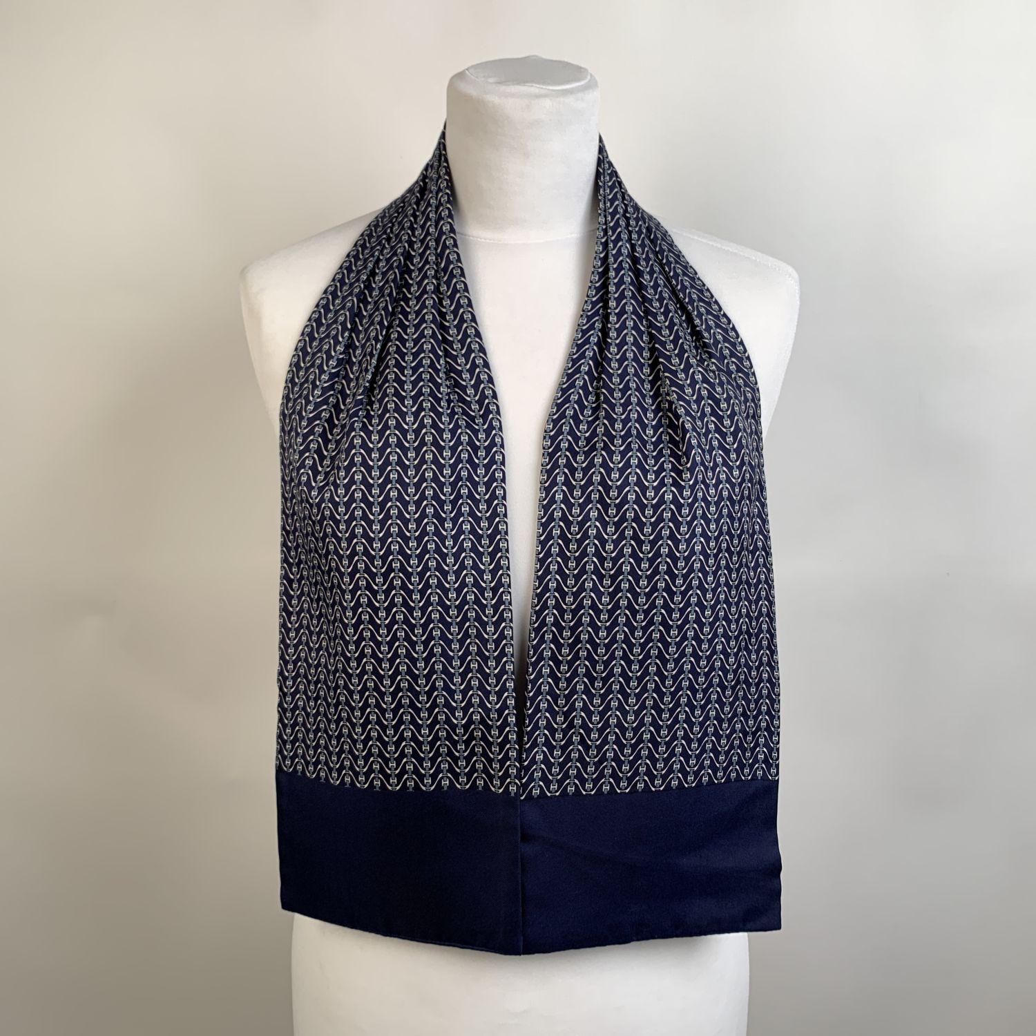 Sophisticated ascot scarf by HERMES, featuring H/buckle pattern on blue background. Pleated,stitched center section. Both suitable for man or woman can be worn in many different ways: as an ascot, at neck, in hair, as a belt or tied on your bag.