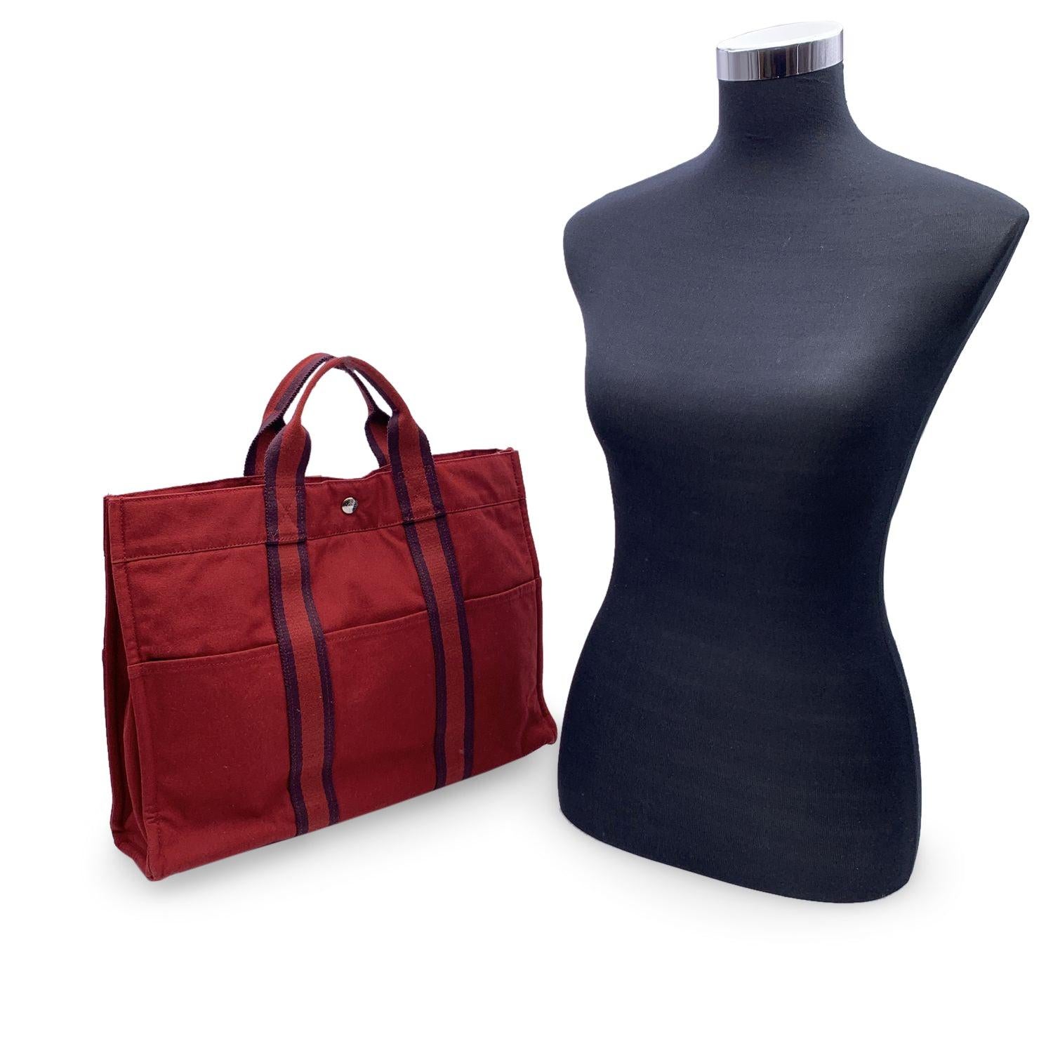 Hermes Paris Vintage red cotton canvas tote, Fourre Tout MM. Made in France. Red color with contrast stripes. 100% Cotton. 3 front pockets on the front and 3 pockets on the back. It has snaps (buttons) on both ends for expansion. Durable canvas