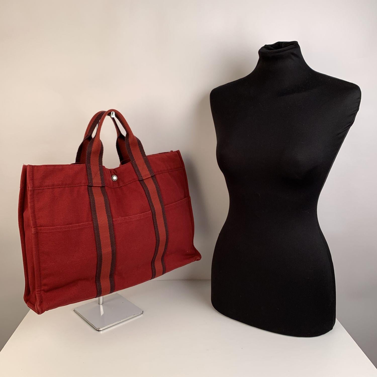 Hermes Paris Vintage red cotton canvas tote, Fourre Tout MM. Made in France. red color with contrast striped detailing. 100% Cotton. 3 front pockets on the front and 3 pockets on the back. It has snaps (buttons) on both ends for expansion. Durable