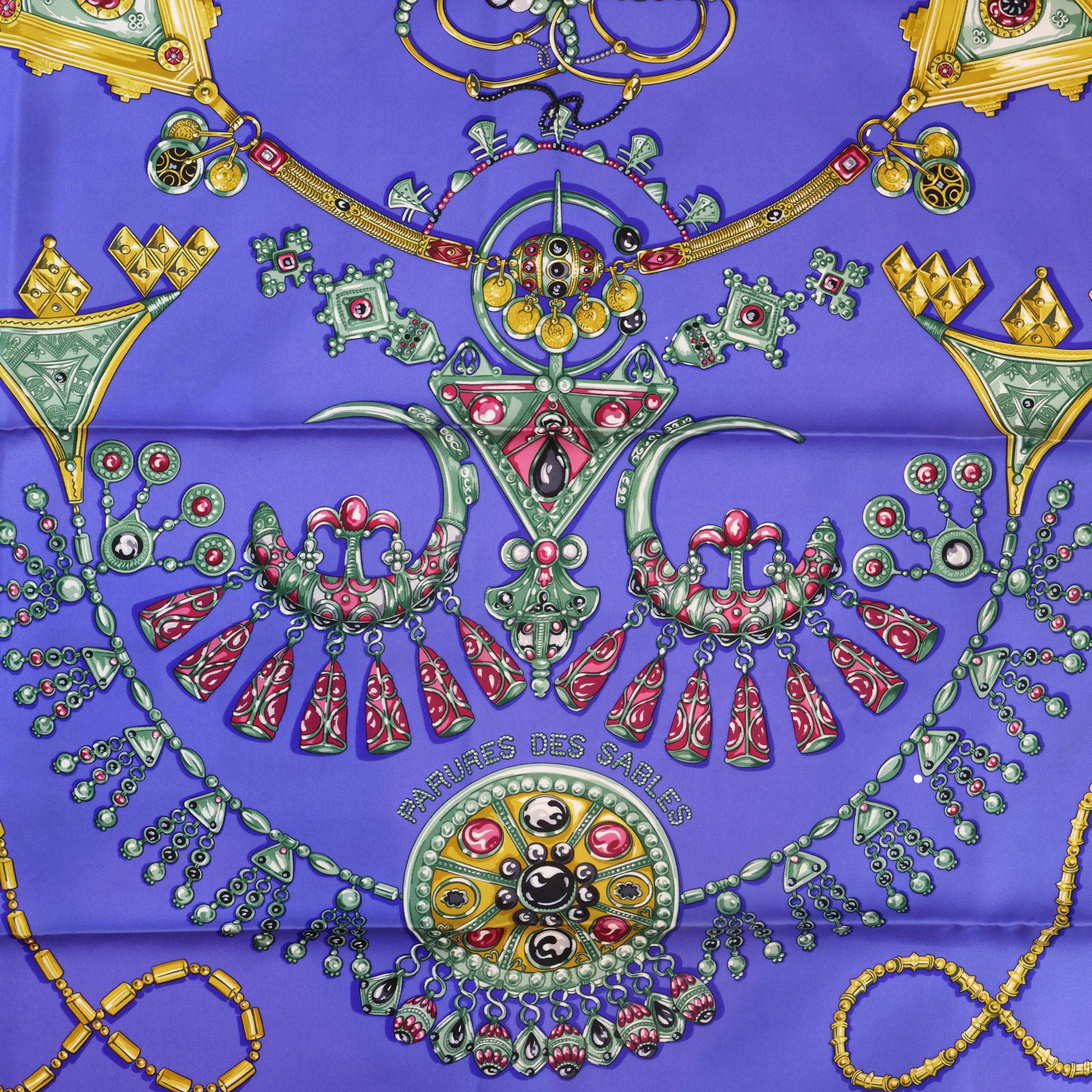 Écharpe en soie Herms « Parures Des Sables » de 90 cm de Laurence Bourthoumieux, 2004. « Paris des Sables », ou « Sand Ornaments » en français, représente une brillante gamme de bijoux rouge et or éclatants sur un fond bleu royal avec une bordure