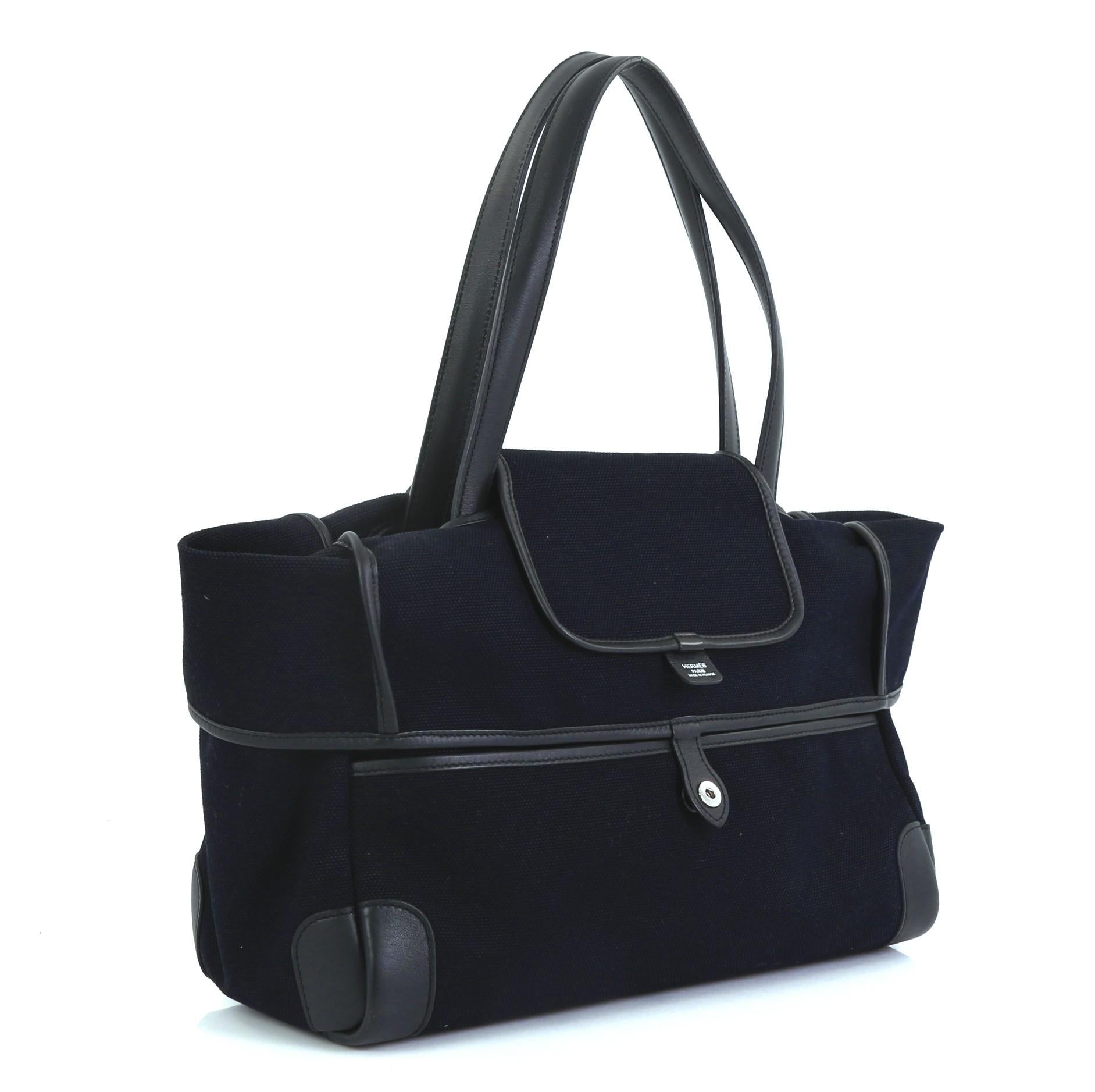 This Hermes Passe-Passe Bag Toile and Leather 35, crafted in Bleu Marine blue Toile Goeland and Noir black Swift leather, features tall flat leather handles and palladium hardware. Its top flap snap closure opens to a Bleu Marine blue Toile Goeland